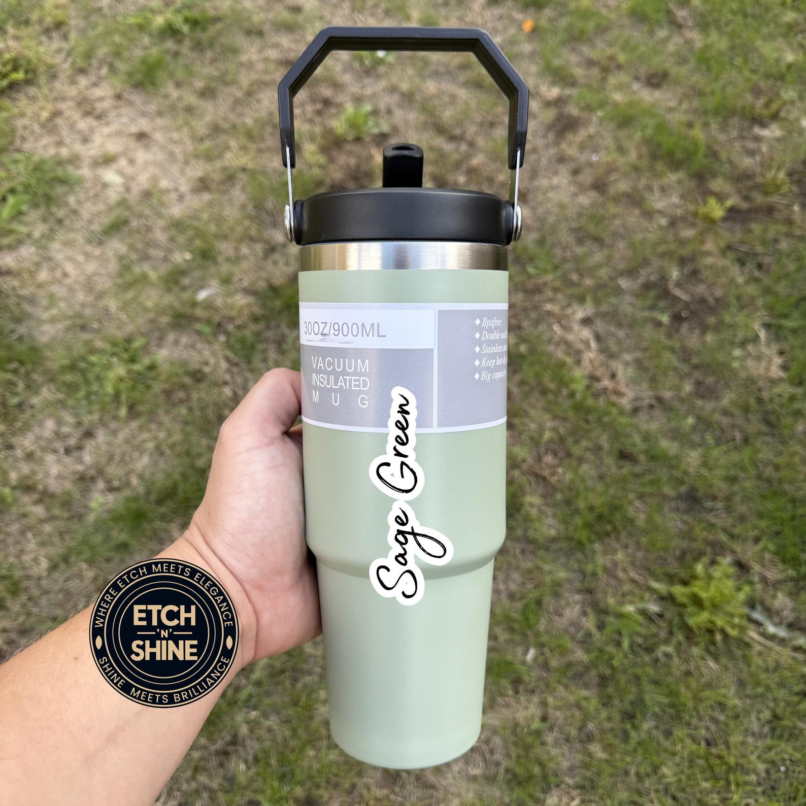 Sage green insulated bottle held in a hand with grass background