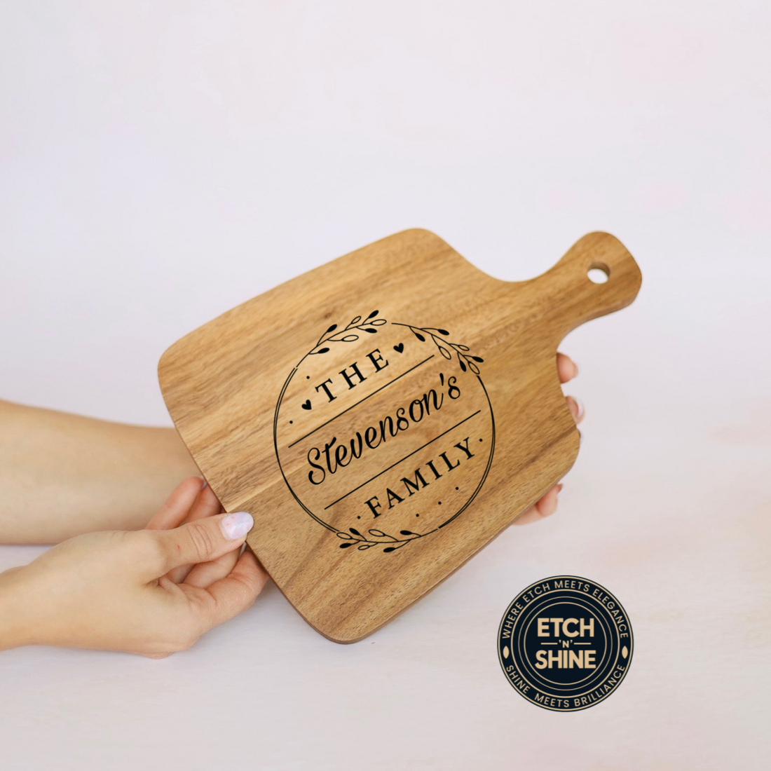 Wooden cutting board with engraved 'The Stevenson's Family' design held by a hand on a light background.