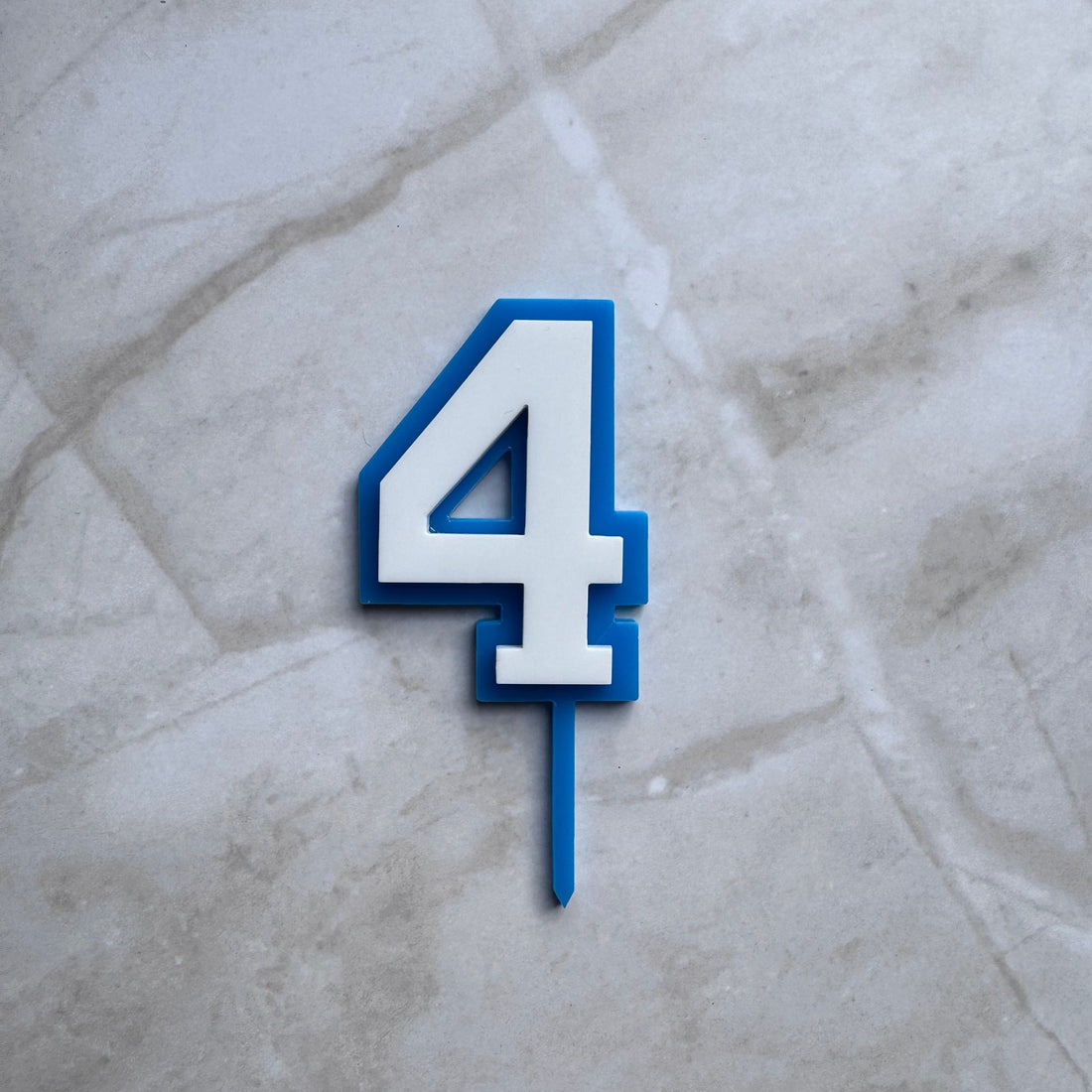 Blue and white double layer acrylic number 4 cake topper in a flat lay