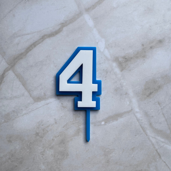 Blue and white double layer acrylic number 4 cake topper in a flat lay