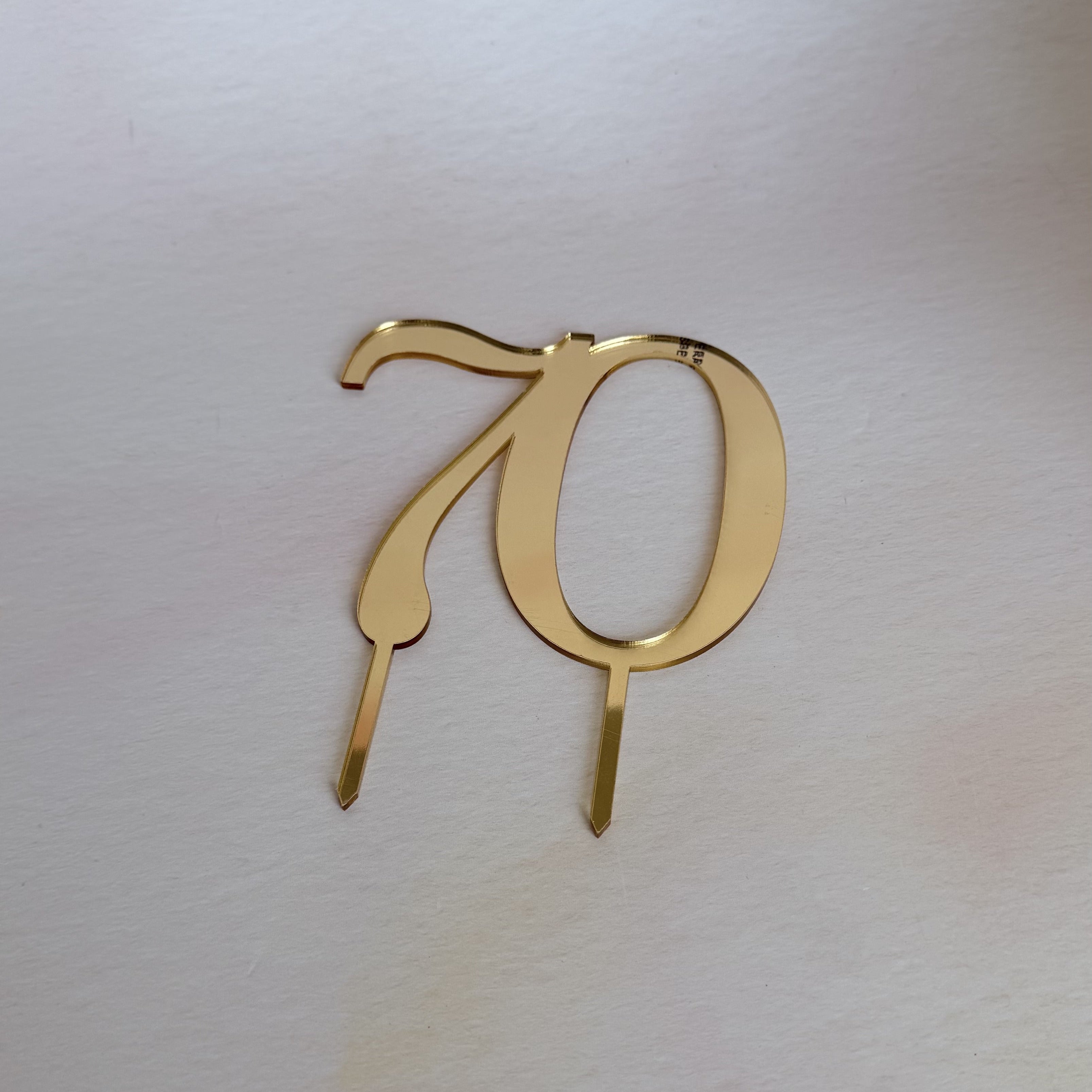 Gold mirror acrylic number 70 cake topper in a flat lay
