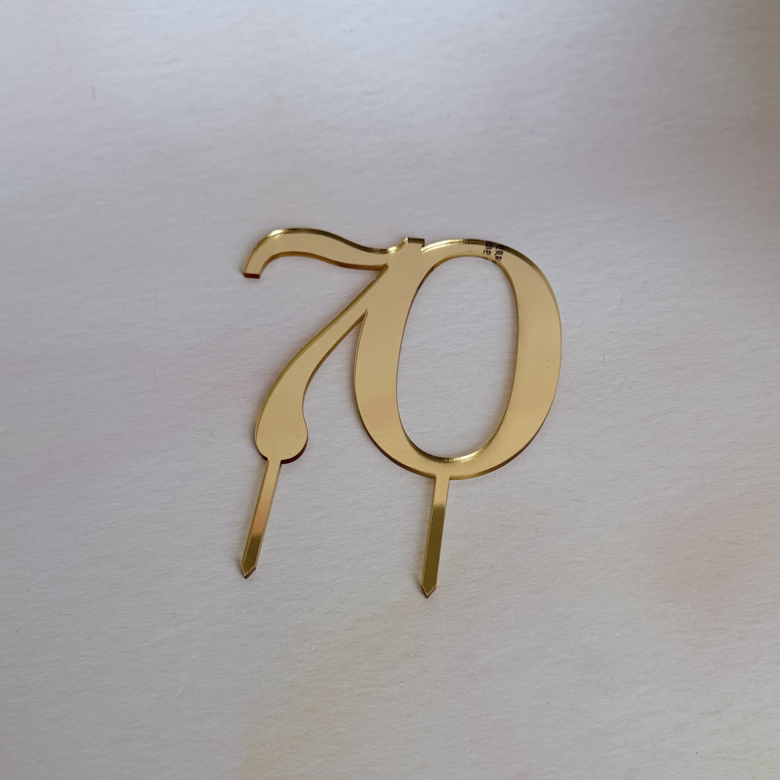Gold mirror acrylic number 70 cake topper in a flat lay