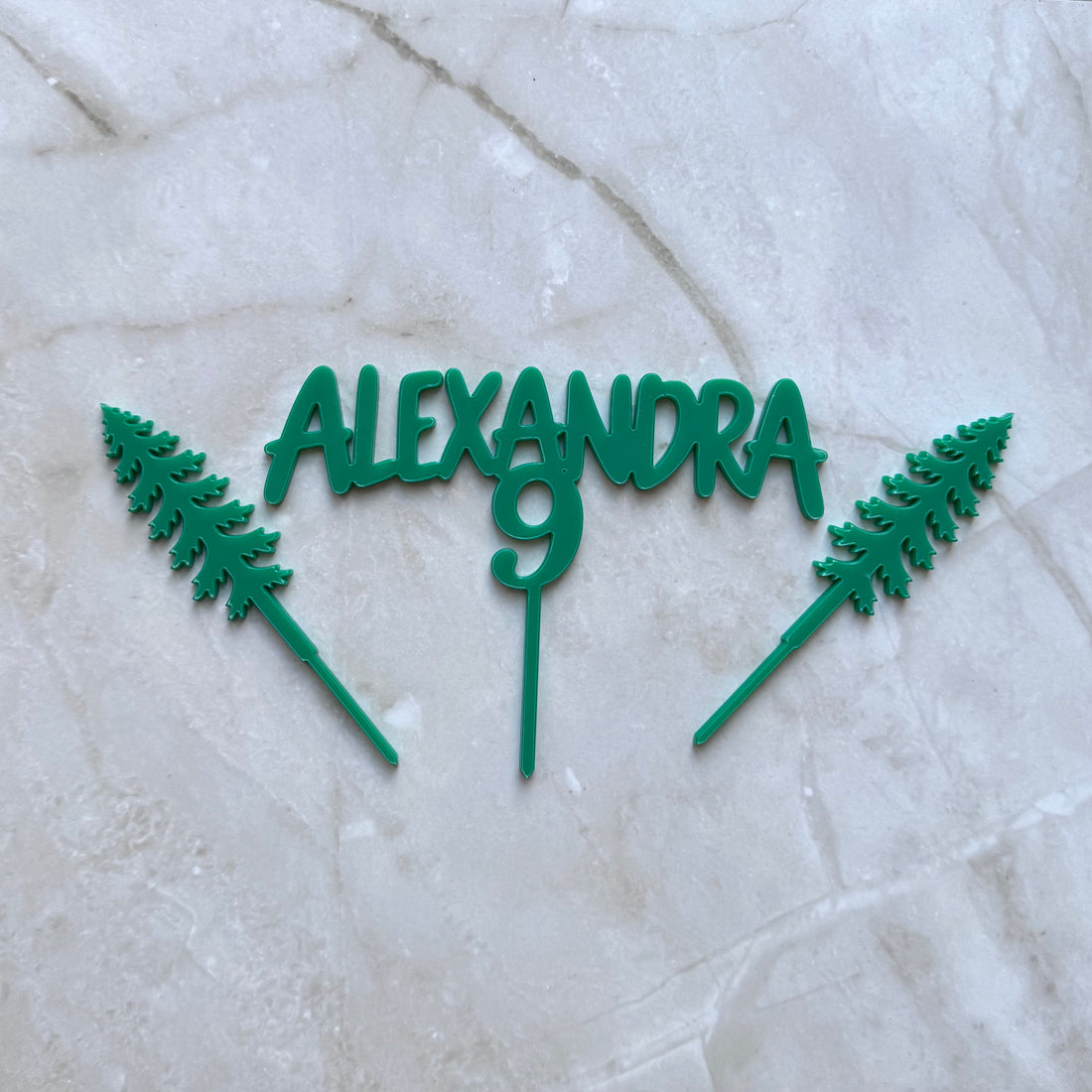 Green personalised number and name acrylic cake topper set in a flat lay