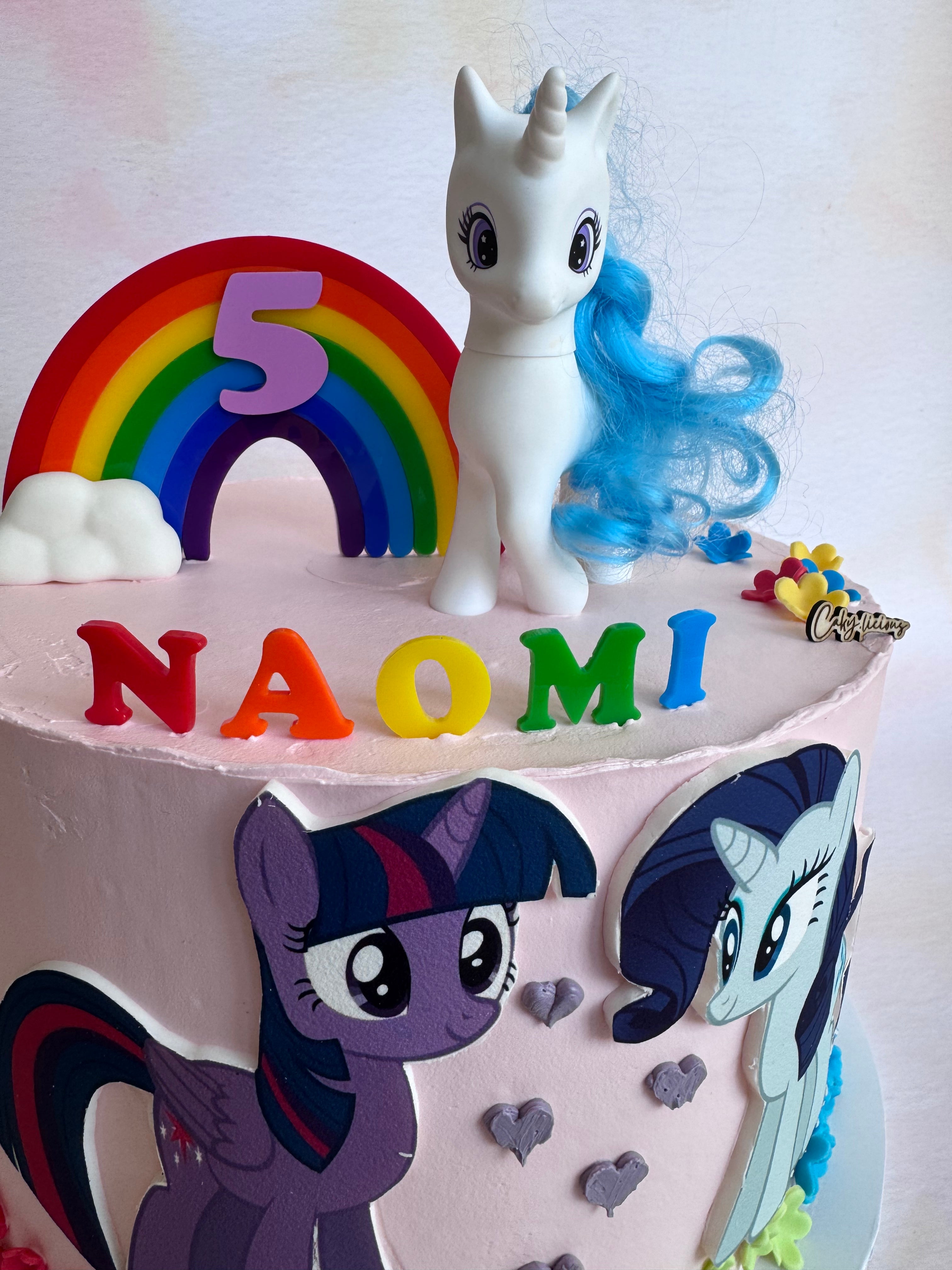 Rainbow arch and NAOMI name topper set on a pink birthday cake, side view – Etch 'N' Shine