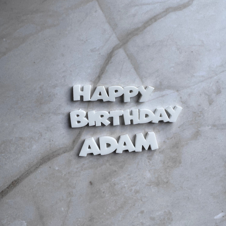 White personalised acrylic Happy Birthday name cake topper in a flat lay
