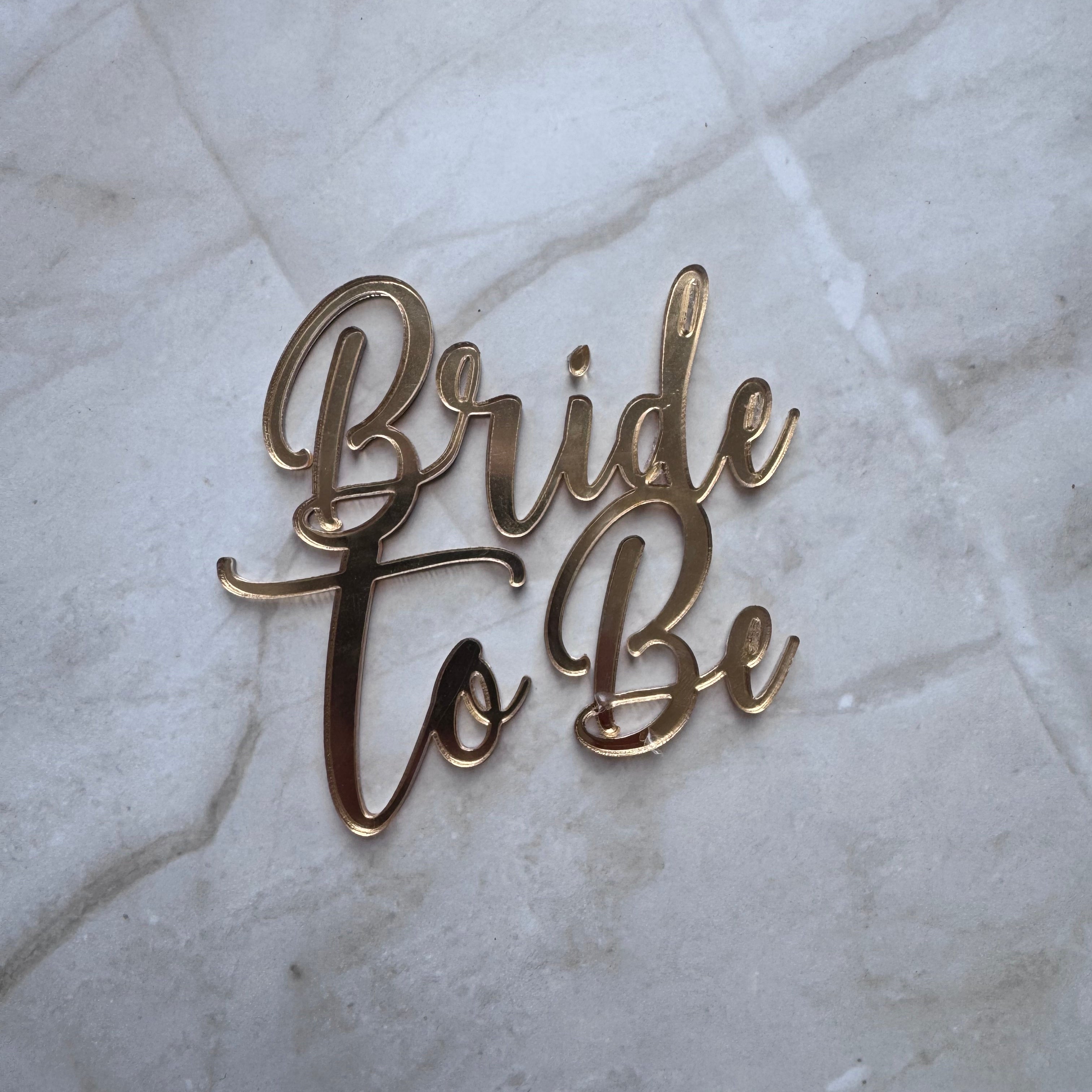 Gold metallic script lettering reading 'Bride to Be' placed on a light marble surface.