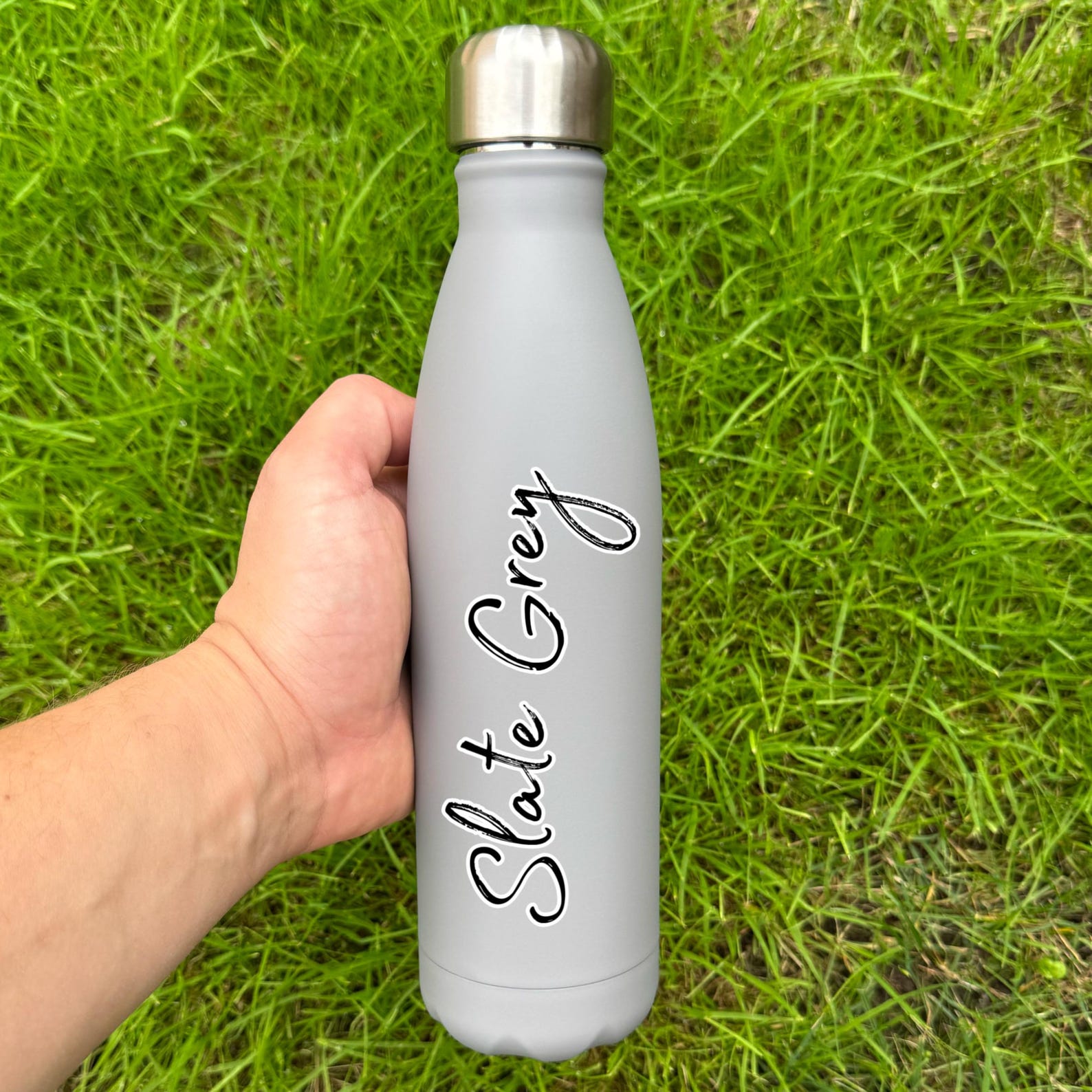 Slate grey water bottle with 'Slate Grey' text held in a hand against a grass background