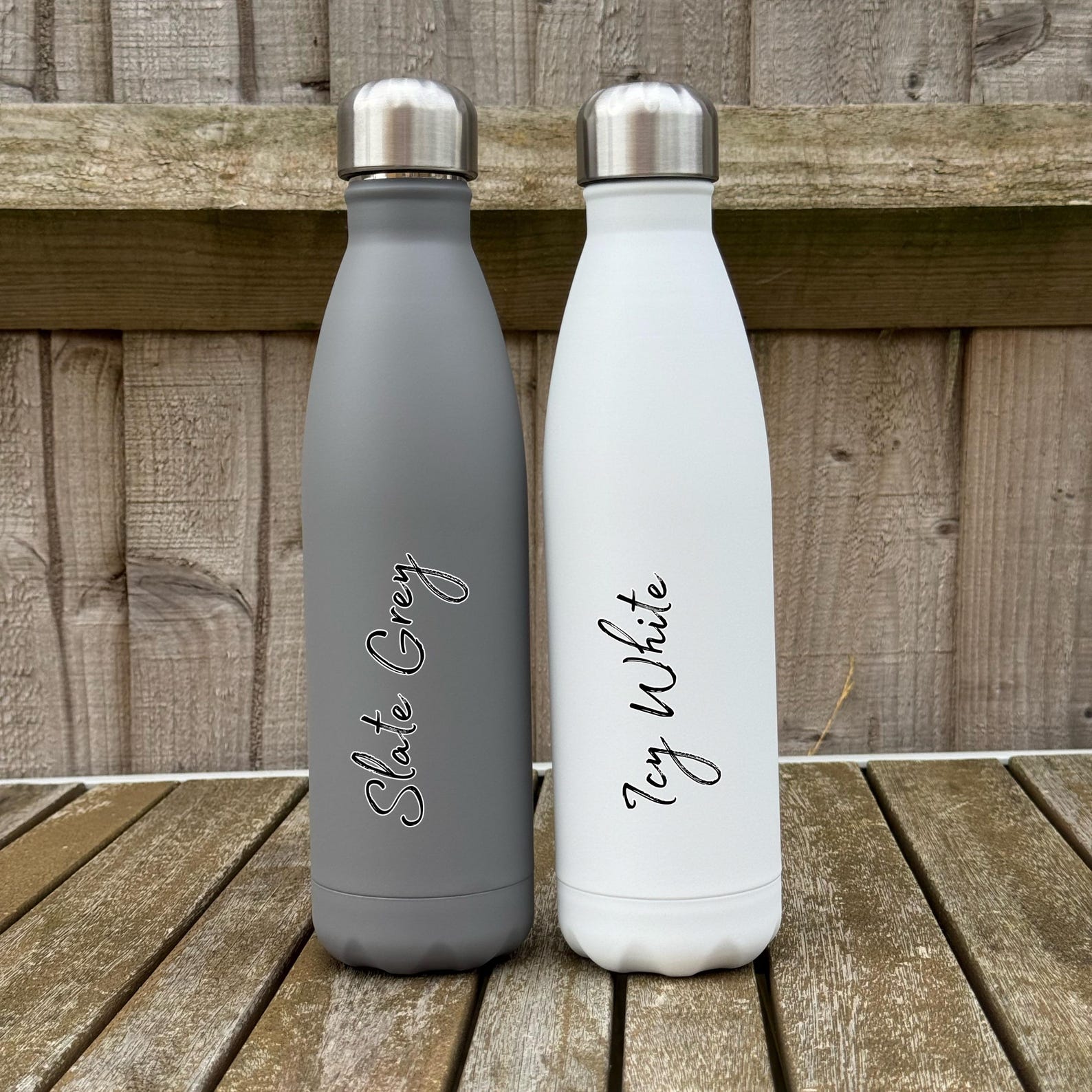 Two insulated bottles, one slate grey and one white, on a wooden surface.