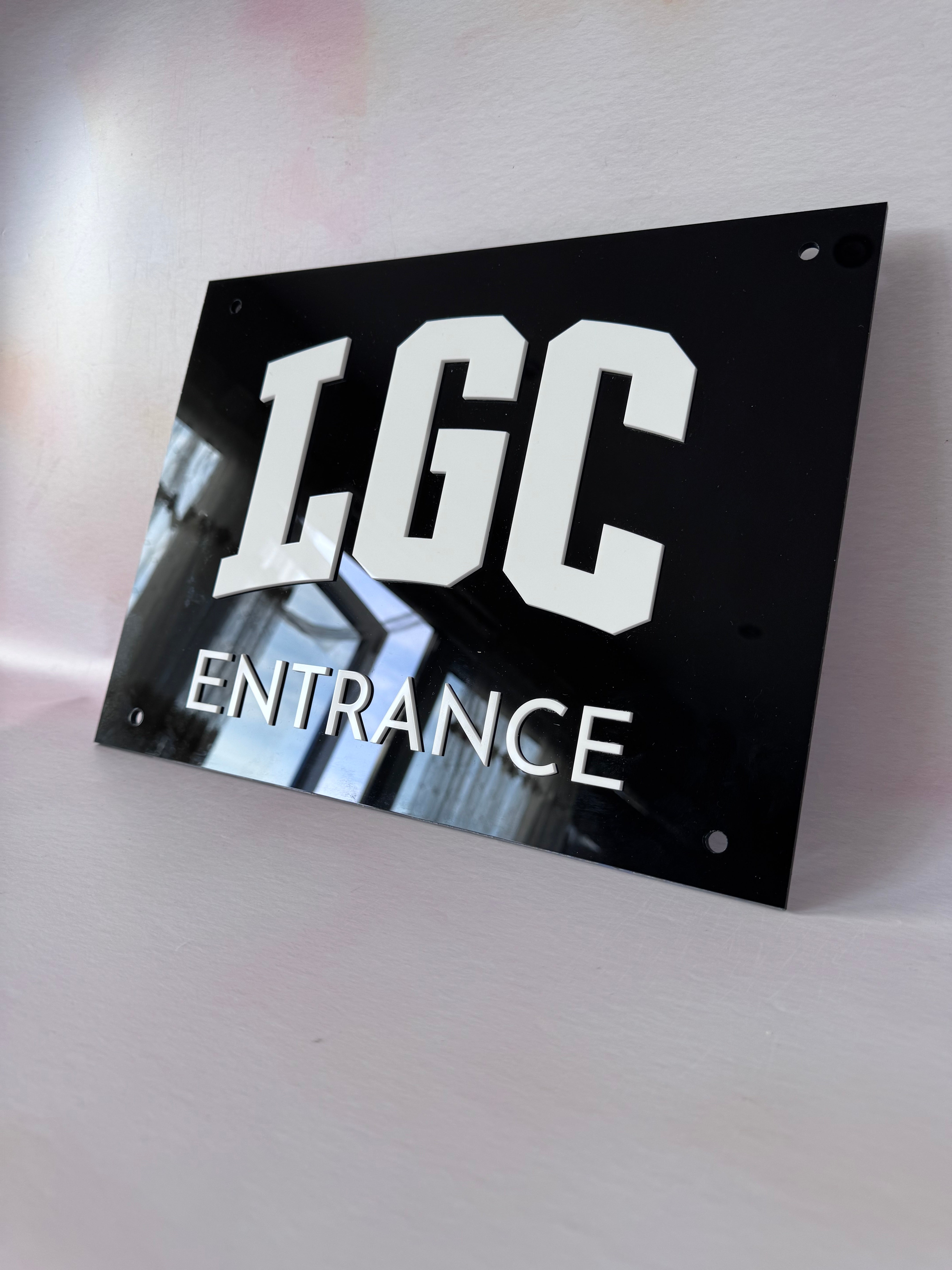 Black acrylic entrance sign with layered white LGC lettering
