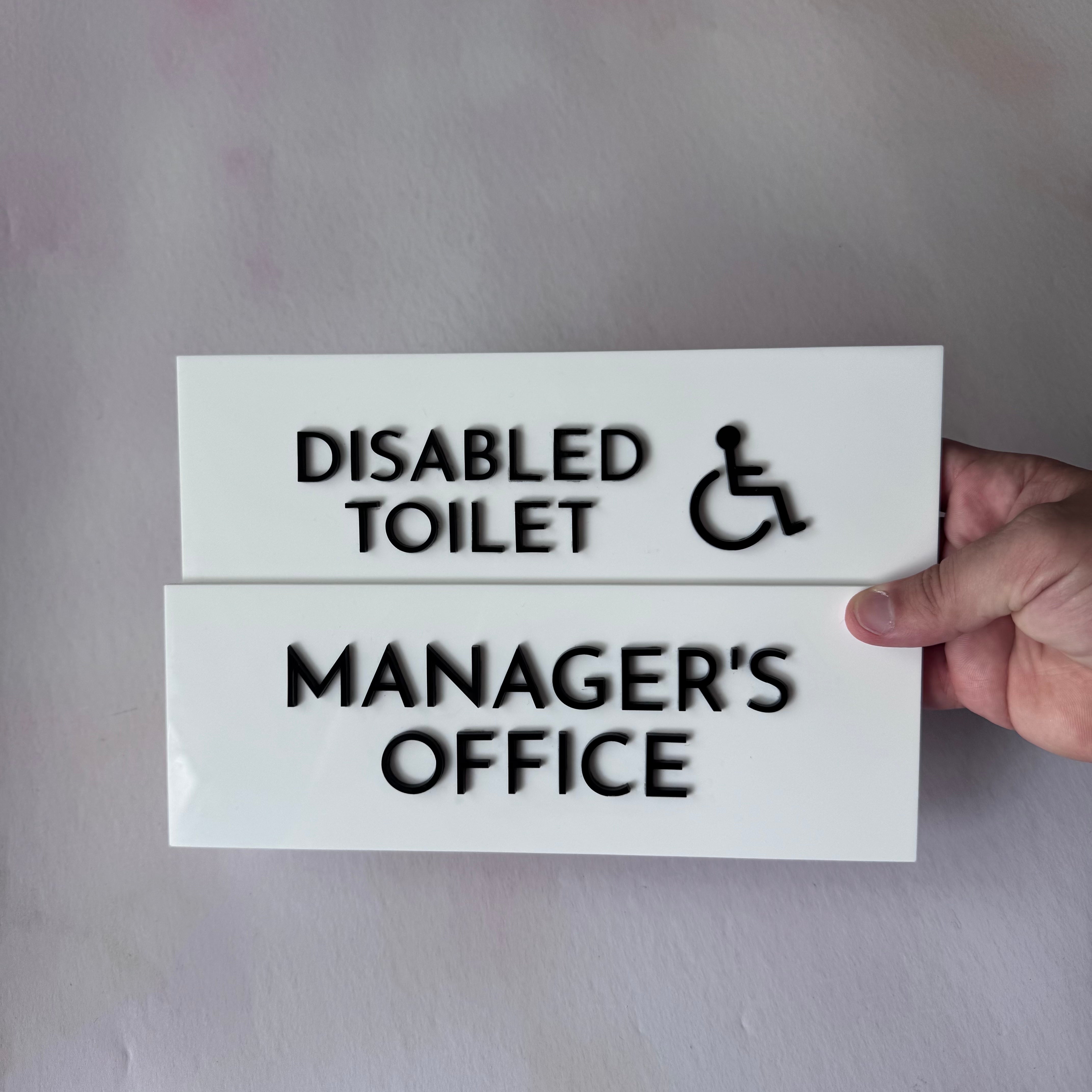 Disabled Toilet and Manager's Office signs held against a wall – white acrylic door signs – Etch 'N' Shine
