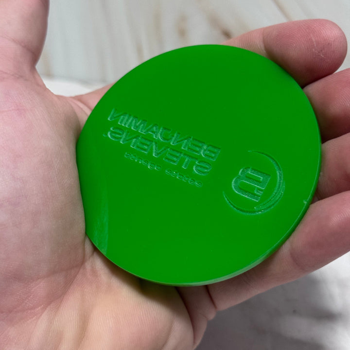 A hand holding a round, bright green product with embossed branding that reads 'MINIVACUUM BENEVESTE' and 'powered by Minivacuum' on a light surface.