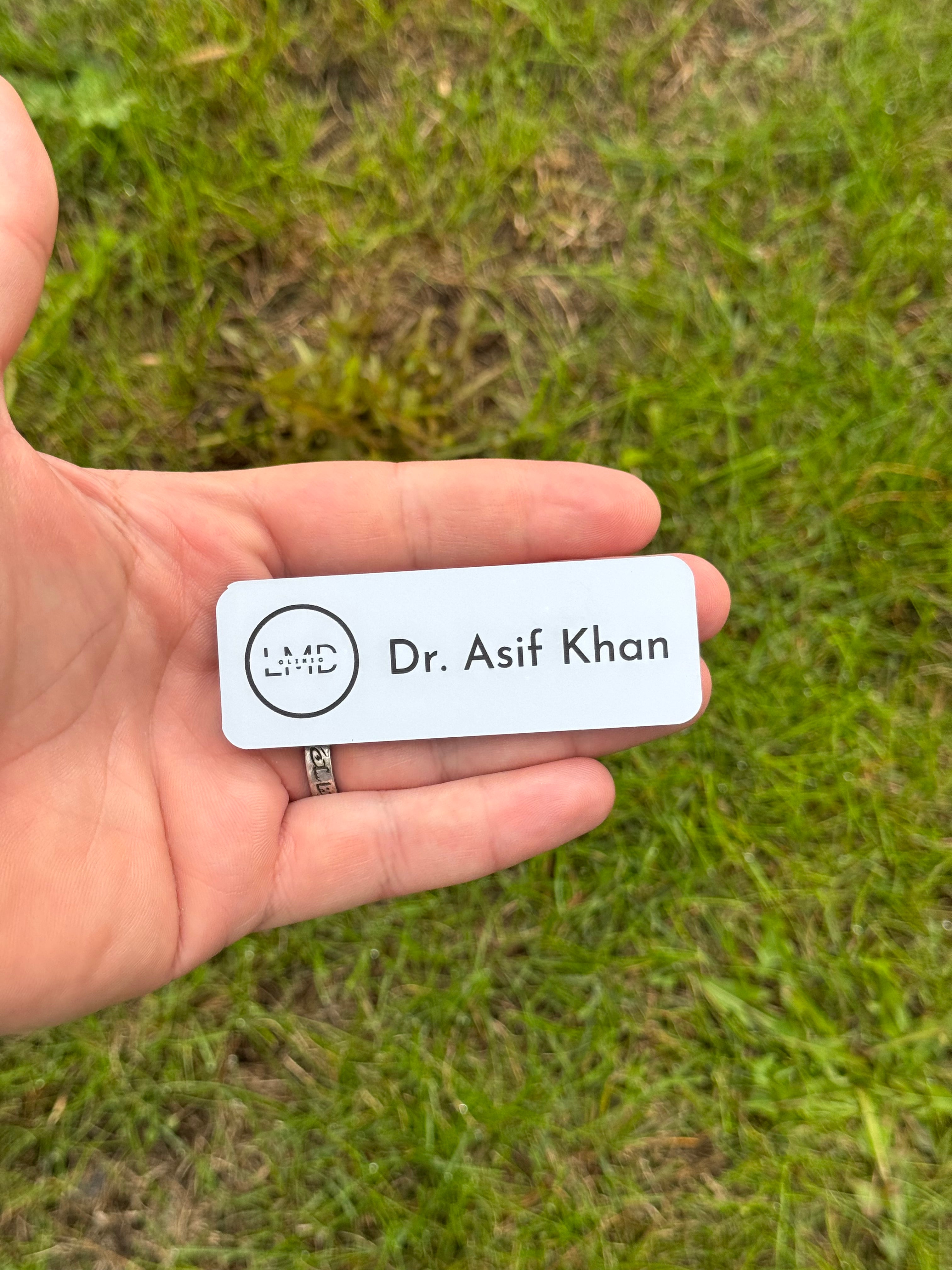 Hand holding a name tag with 'Dr. Asif Khan' on a grassy background