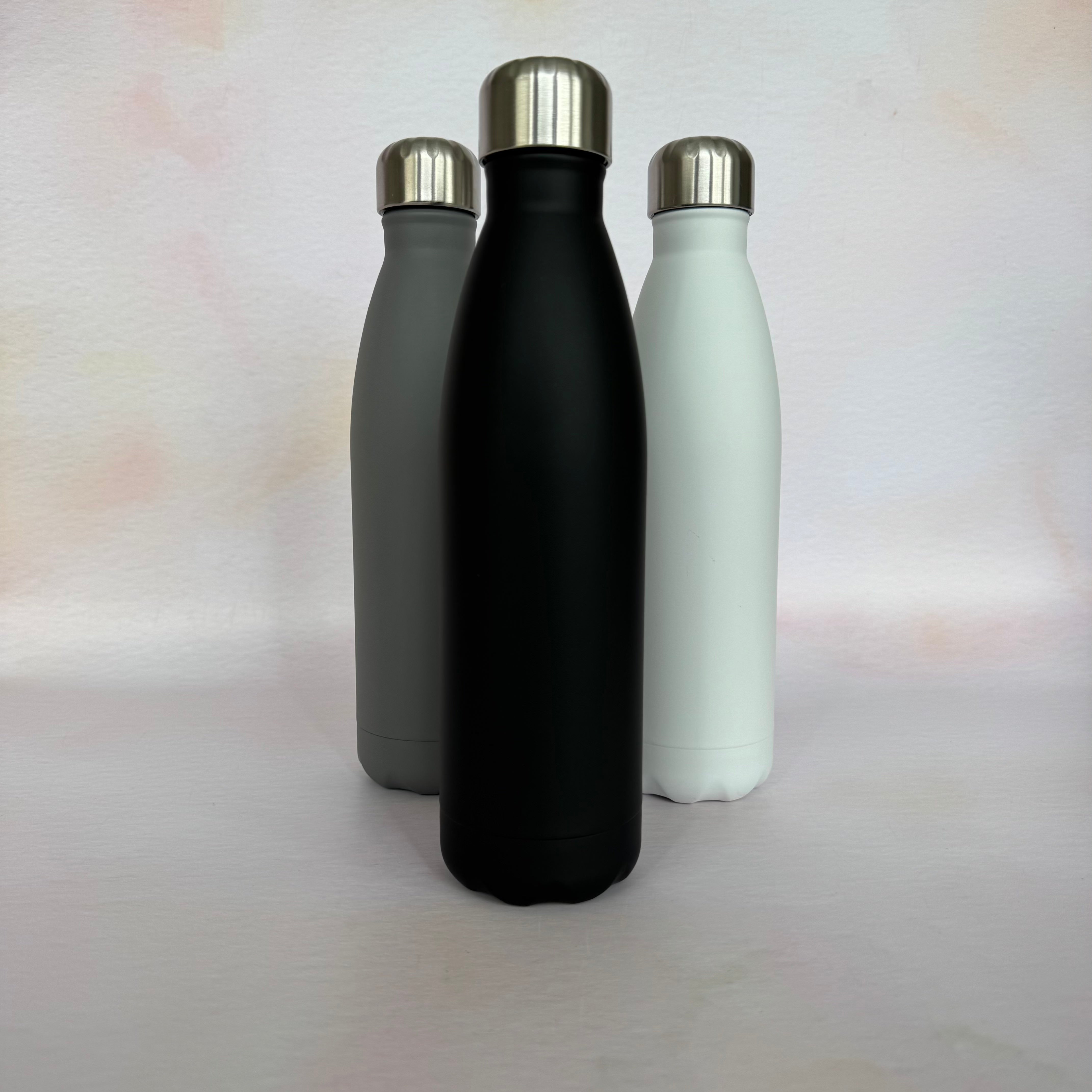 Three insulated bottles in black, gray, and white with silver caps on a light background