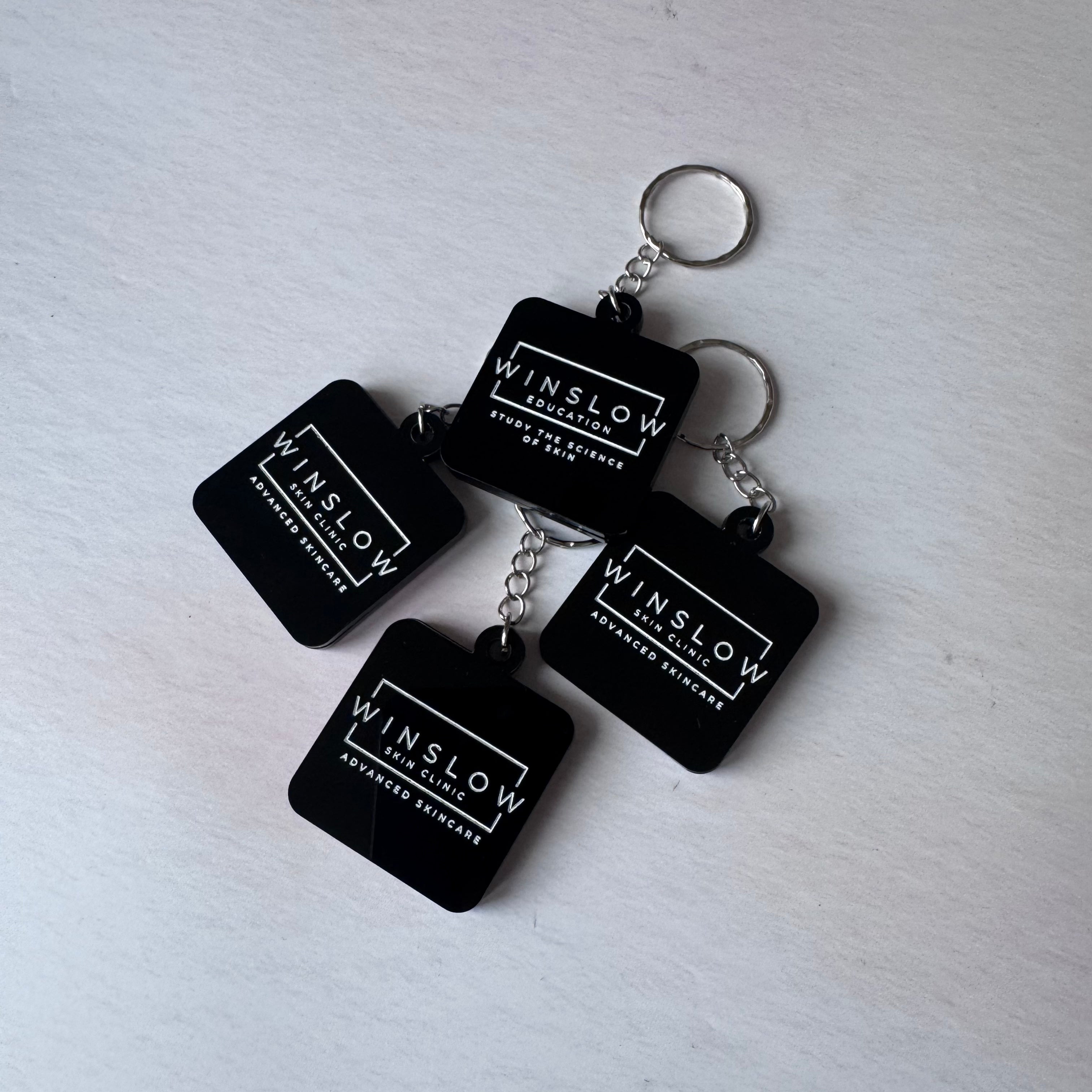 Four black acrylic NFC keyrings engraved with the Winslow Skin Clinic logo, flat lay – Etch 'N' Shine