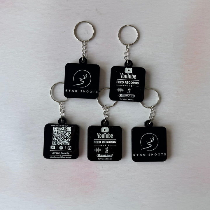 Five black square keychains with silver metal rings, arranged on a light off-white surface. Each keychain has a small rectangular black tag printed with white text and logos, including 'YouTube', 'FRED RECOORDS', and 'STAR SHOOTS'.