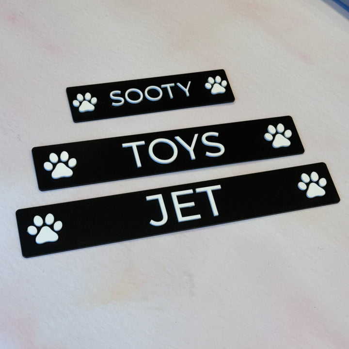 Black layered acrylic pet name plaques with raised white names and paw icons