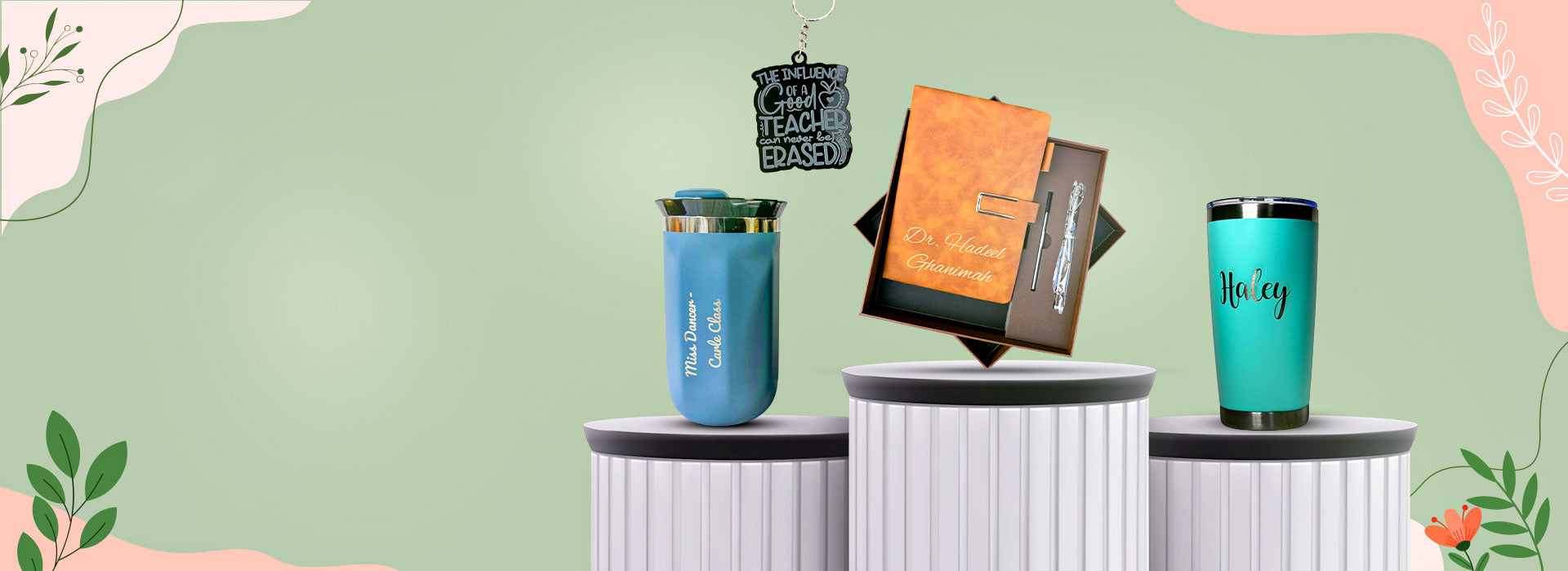 Two blue tumblers on white cylindrical stands with a decorative green and pink background.