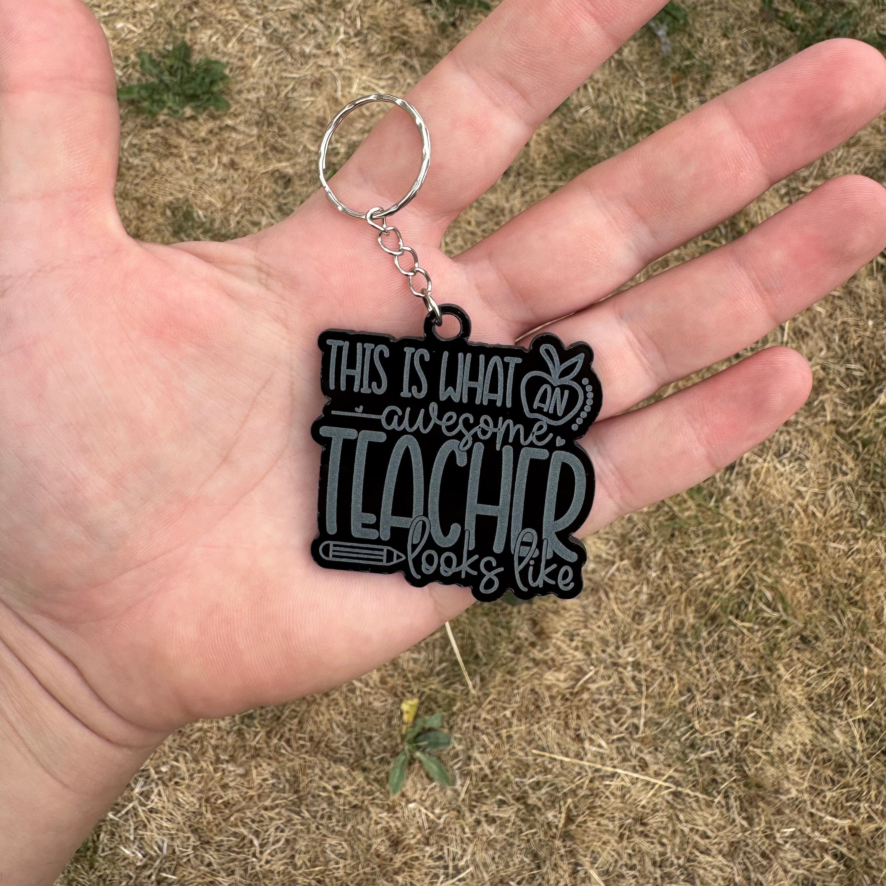 Glossy black personalised teacher keychain reading ‘This is what an awesome teacher looks like’ held in hand – ideal gift for educators