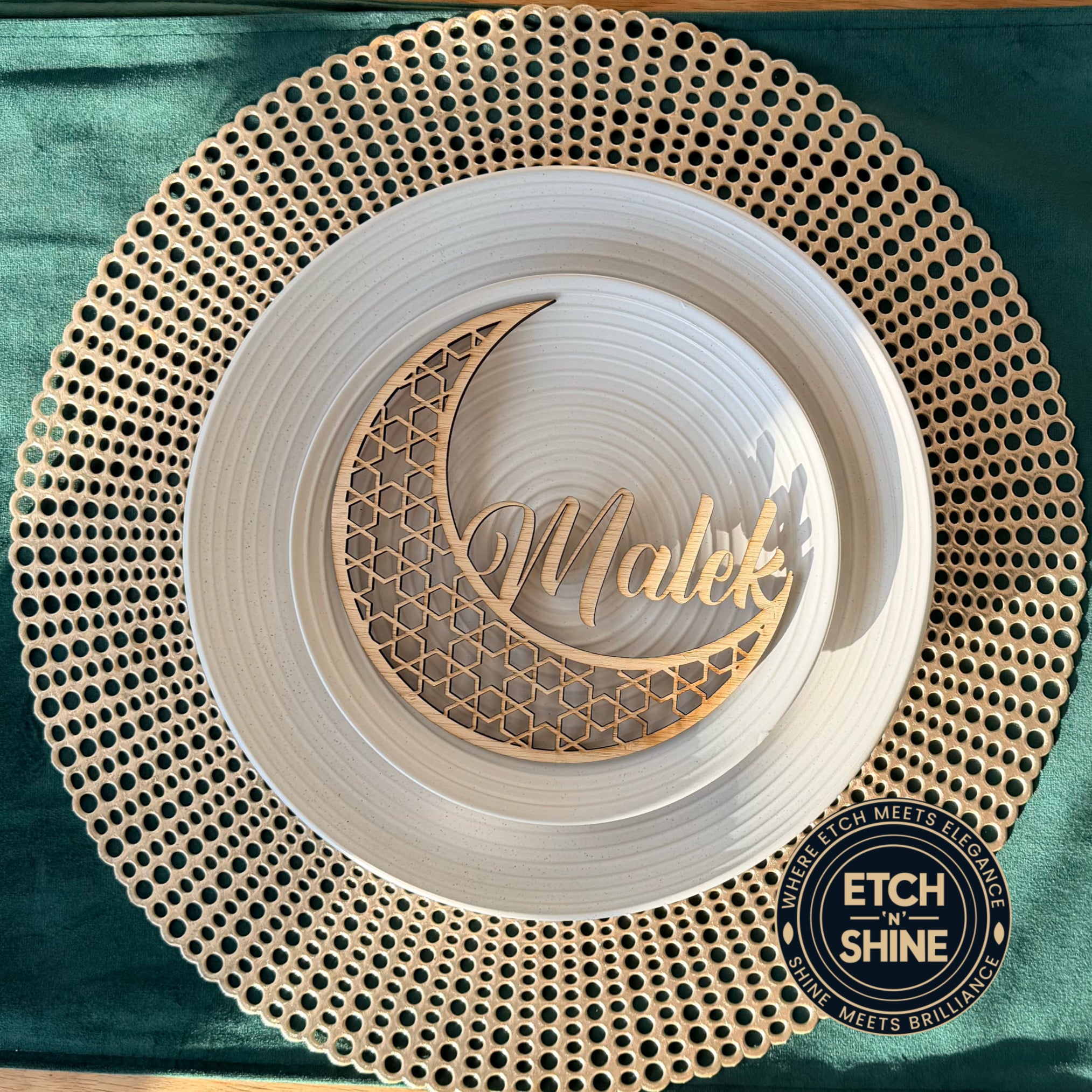 Decorative plate with 'Malek' engraving on a textured gold rim against a teal background