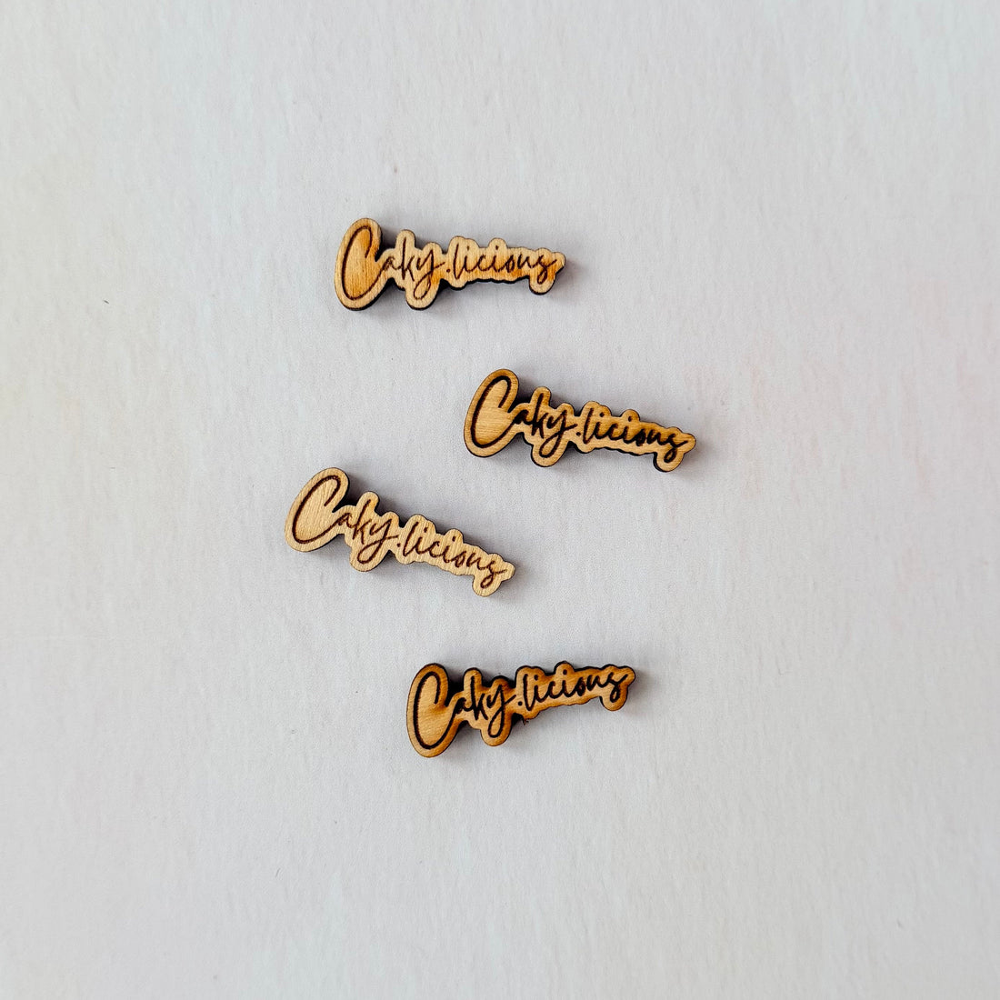 Four wooden 'cackylicious' cake tags for cake branding white background