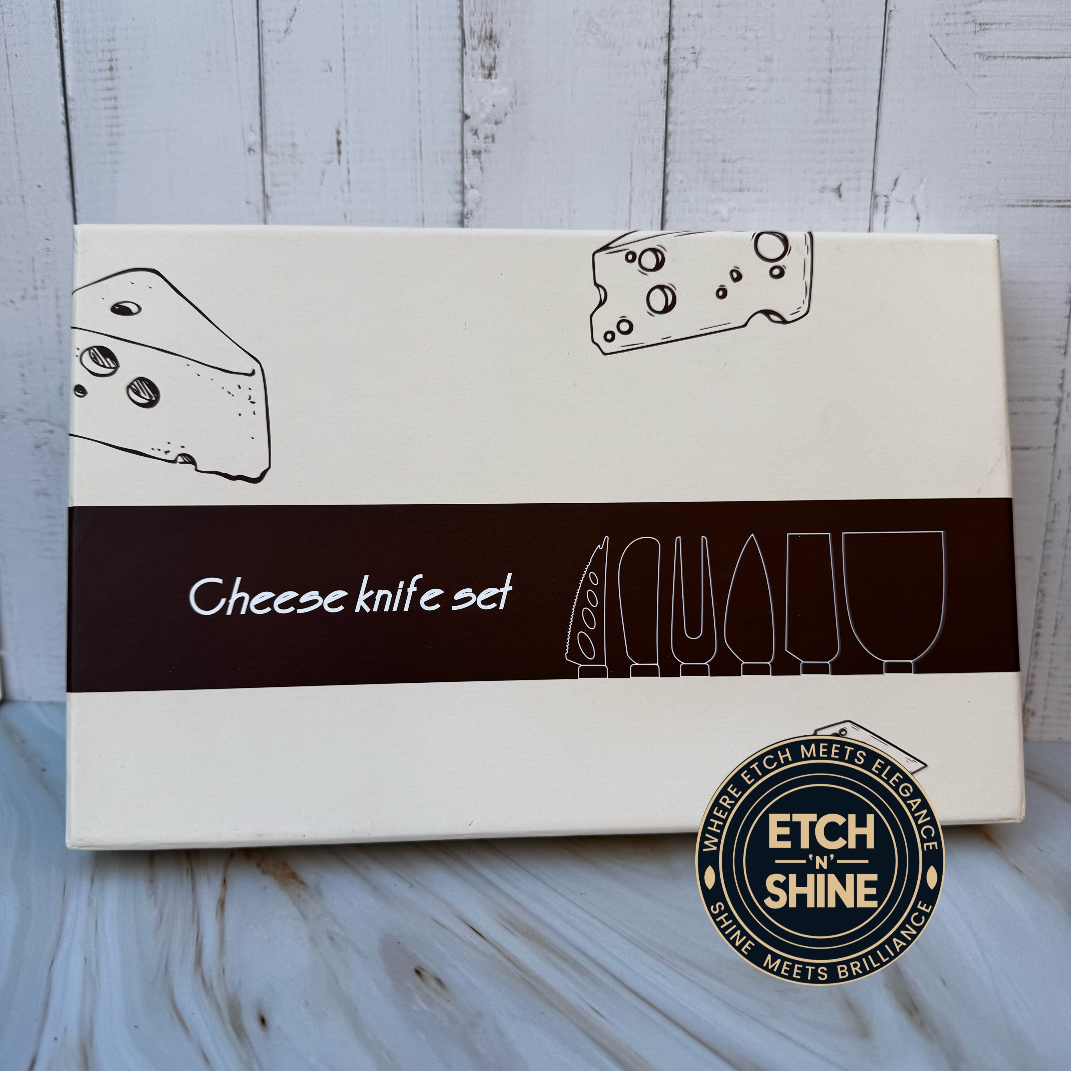 Box for a cheese knife set with illustrations of cheese and knives on a wooden surface.