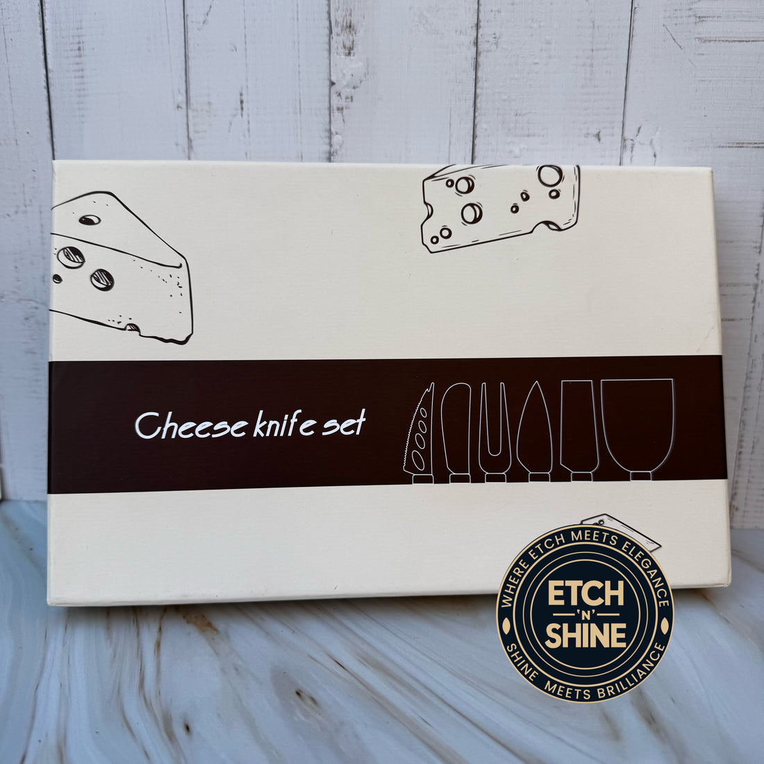 Box for a cheese knife set with illustrations of cheese and knives on a wooden surface.