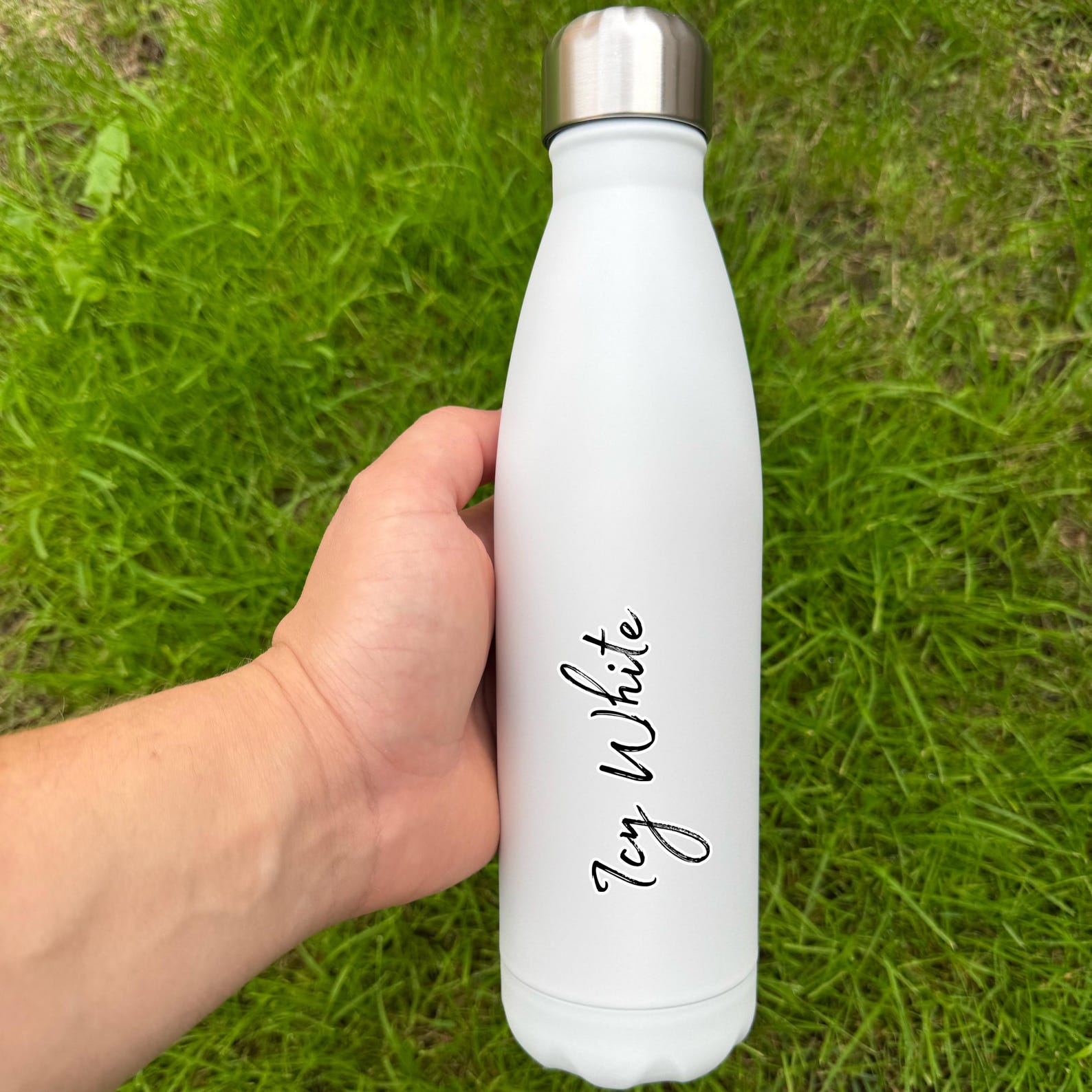 White water bottle with 'Icy White' text held in a hand on grass