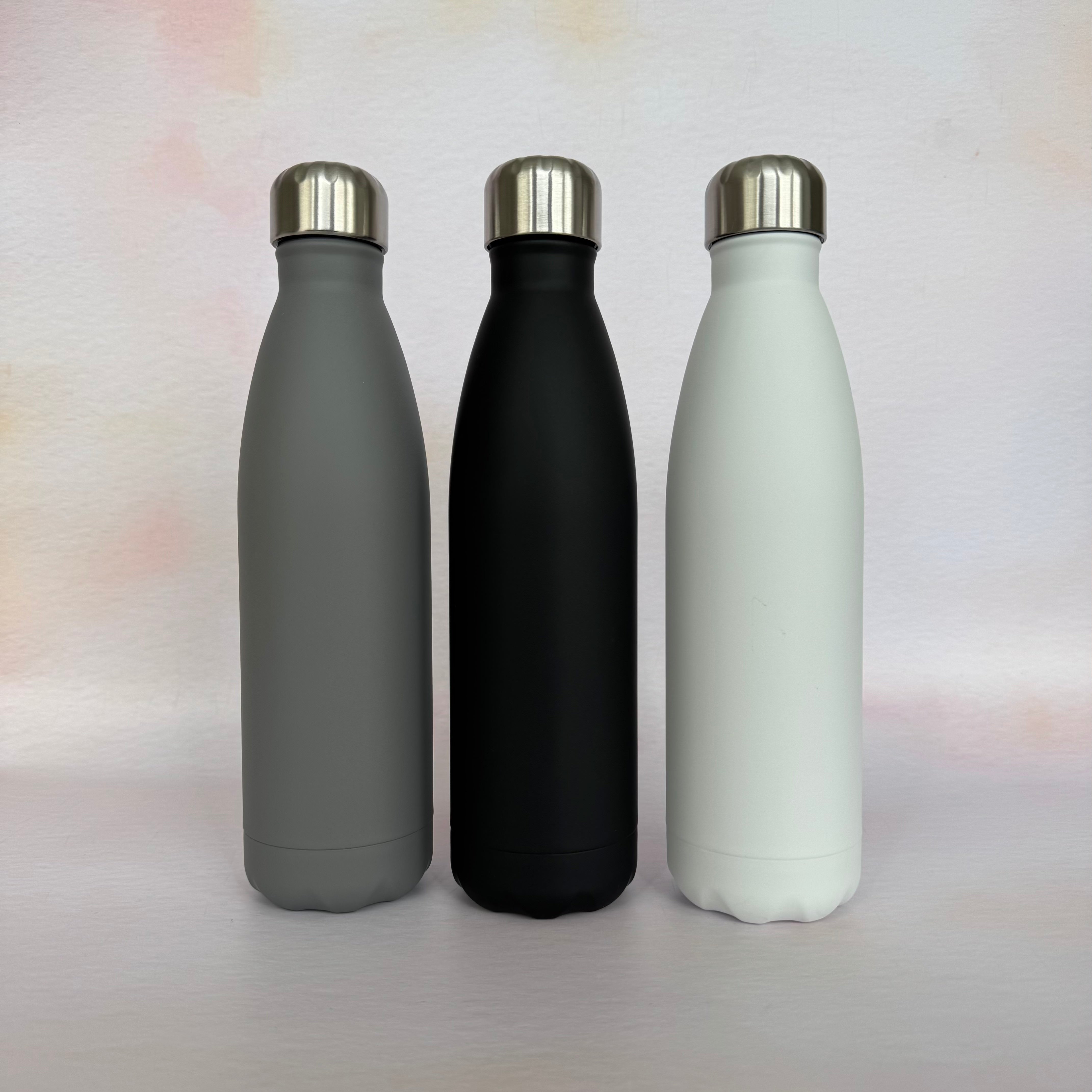 Three insulated bottles in gray, black, and white on a light background