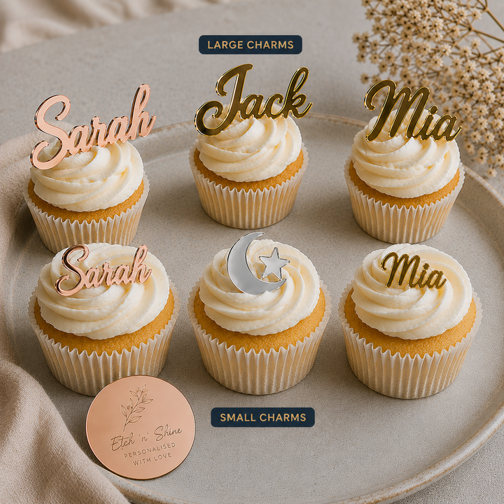 Six frosted cupcakes arranged on a beige plate, each topped with a custom name charm in rose gold or gold script. The cupcakes include names like Sarah, Jack, and Mia, and one has a crescent moon and star charm.