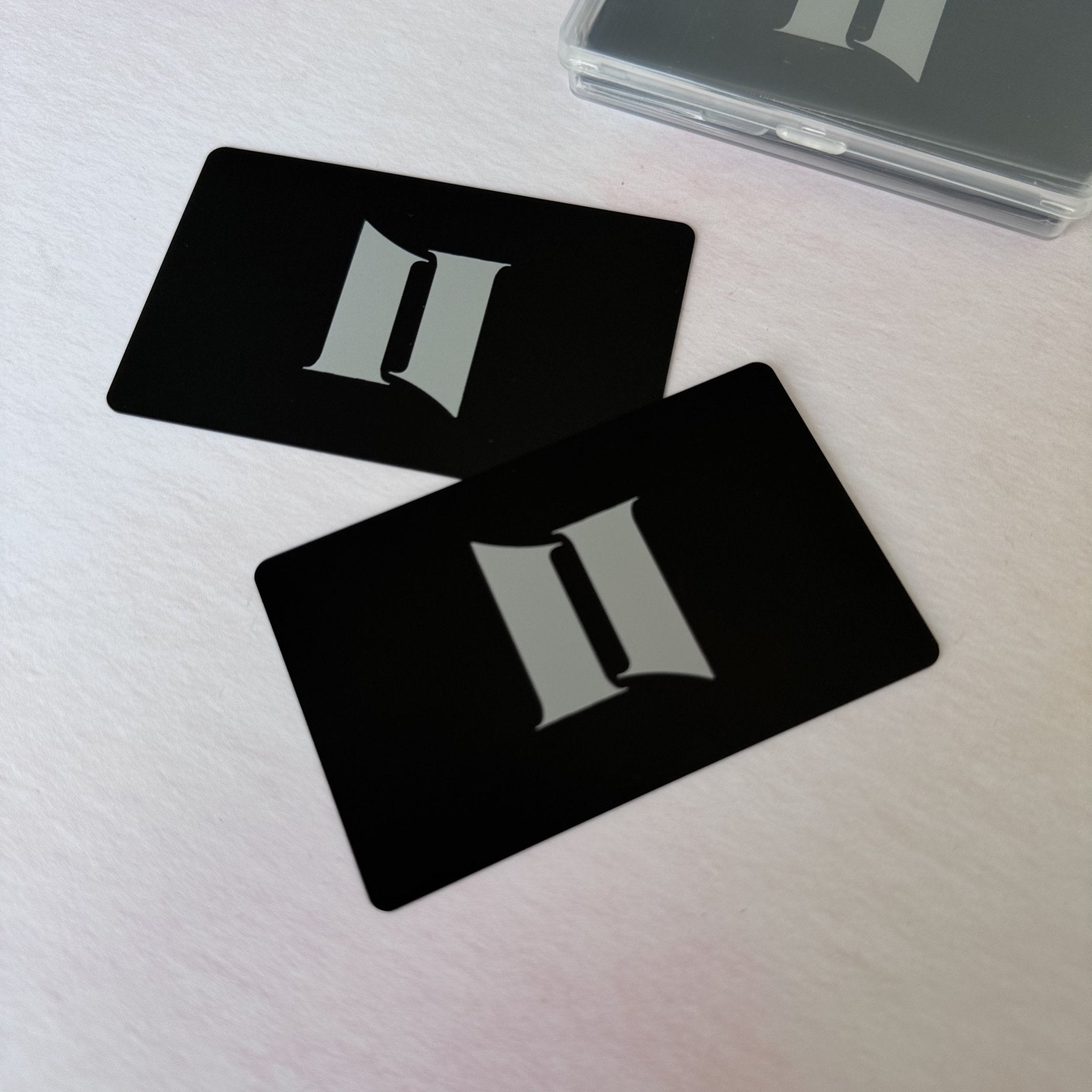 Two black metal cards with engraved initials beside clear case – engraved aluminium business cards – Etch 'N' Shine