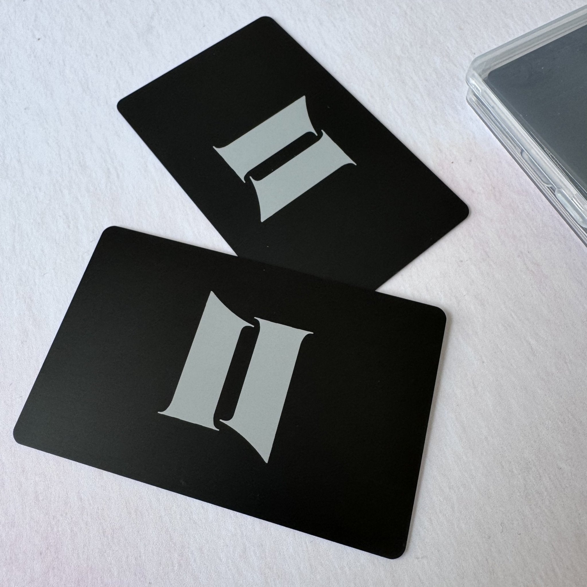 Two black metal cards with engraved initials beside a clear case – personalised metal card – Etch 'N' Shine
