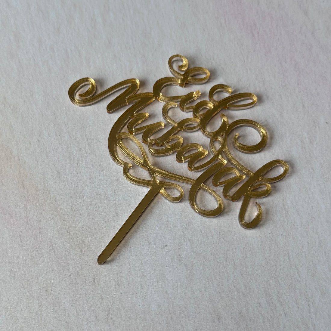 Gold 'Eid Mubarak' cake topper on a white background