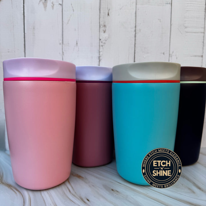 Four colorful tumblers on a wooden surface with 'Etch in Shine' branding.