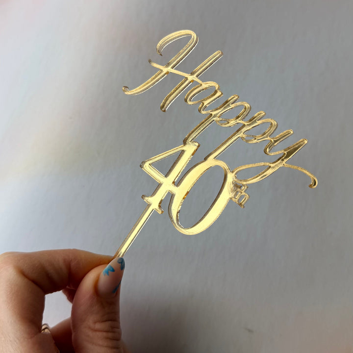 Gold 'Happy 40' cake topper held by a hand against a light background