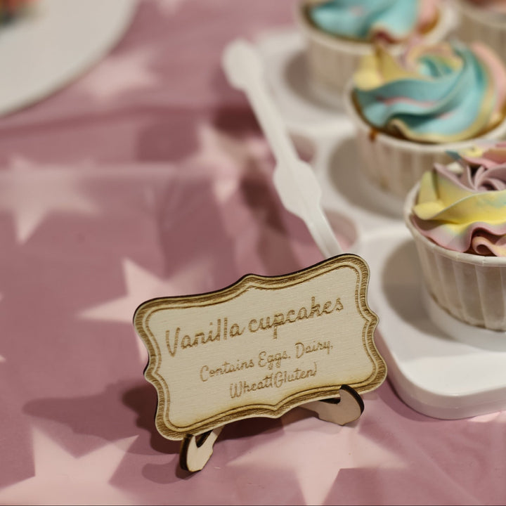 Vanilla cupcakes on a pink tablecloth with a decorative sign.