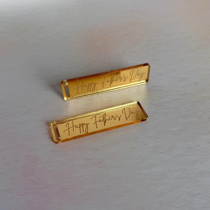 Two gold mirror acrylic tags with engraved text on a white surface