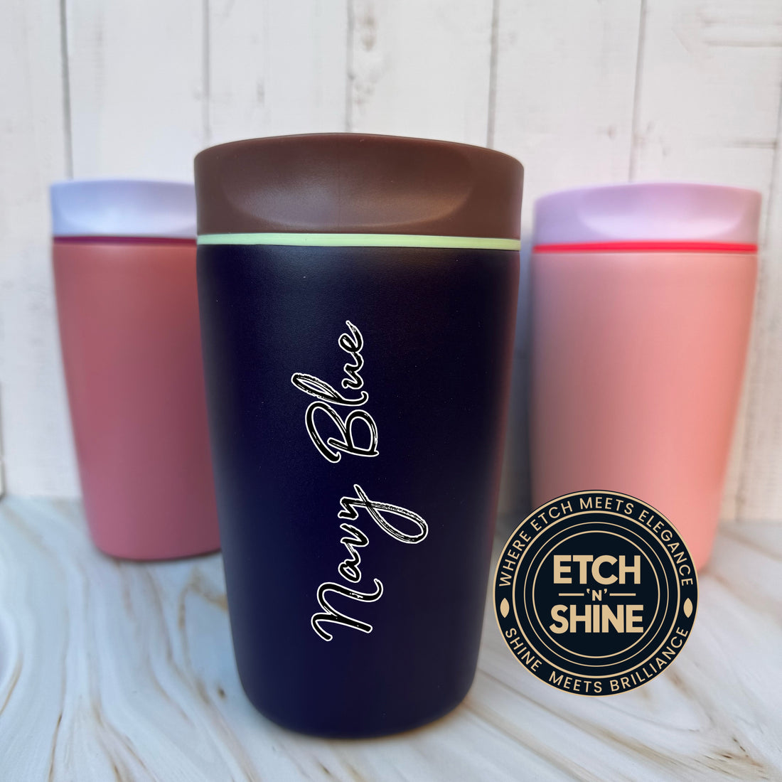 Navy blue tumbler with 'Navy Blue' text, surrounded by pink tumblers on a wooden surface, with Etch 'n Shine logo.