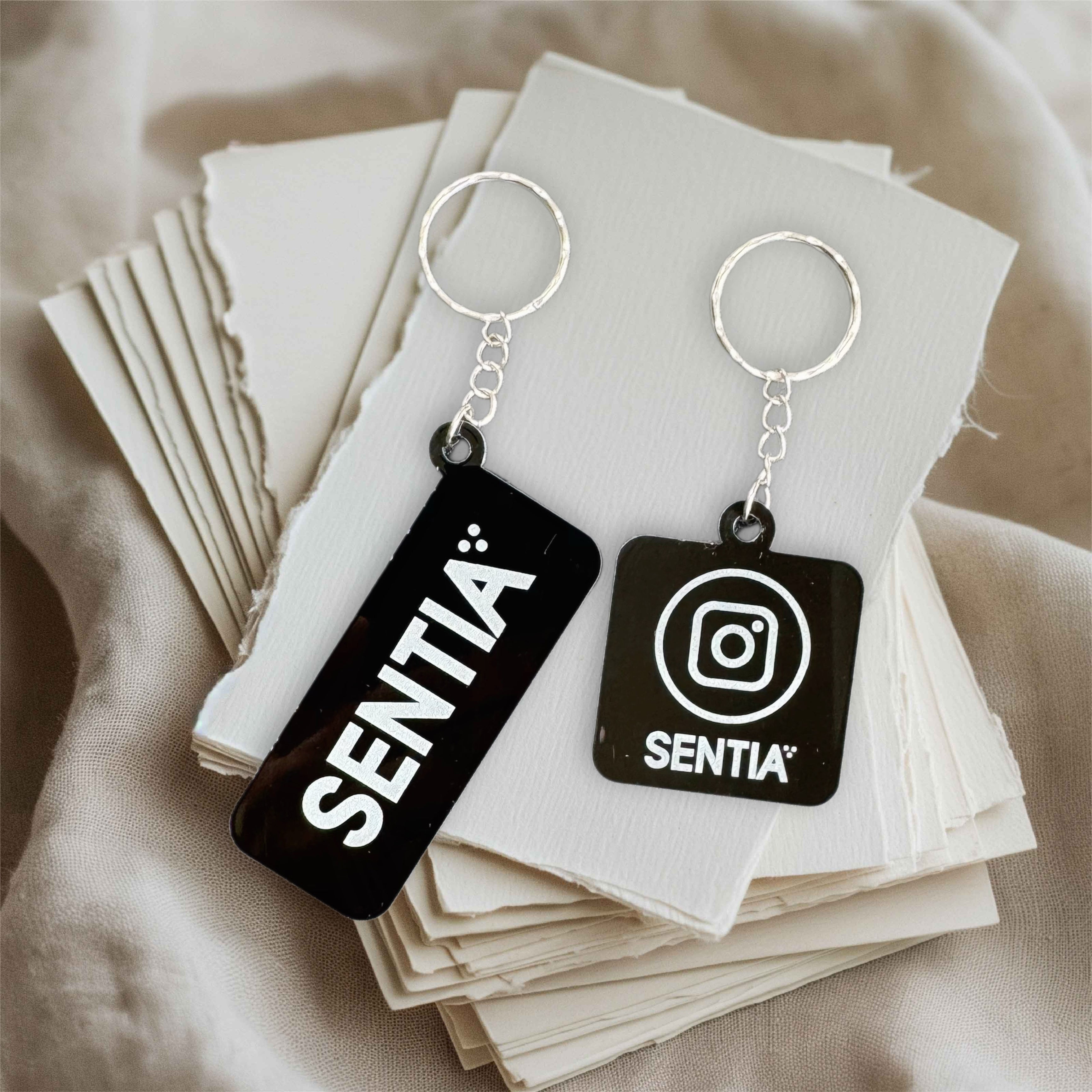 Two custom NFC black acrylic keychains featuring SENTIA logo and Instagram icon – tap to link smart business keychains