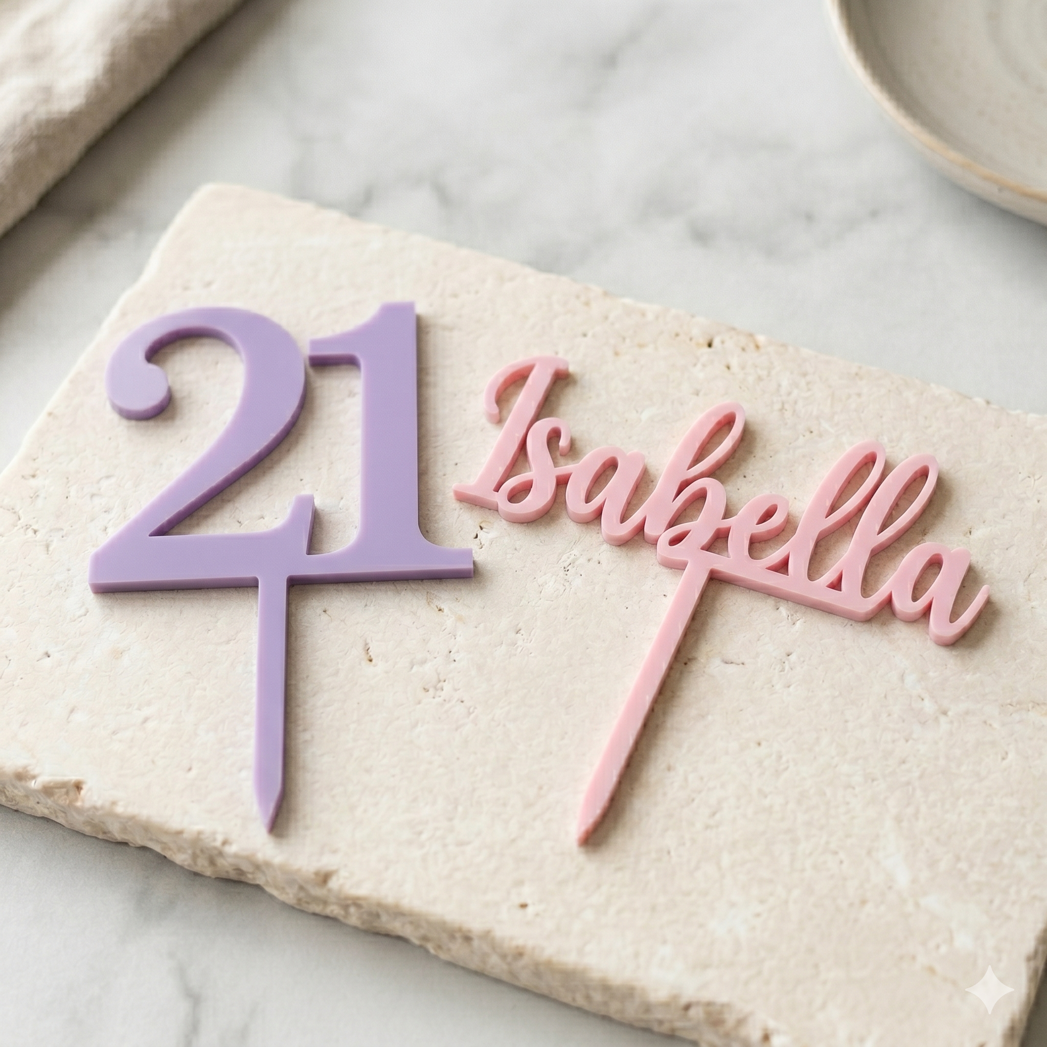 Decorative cake topper with '21' in purple and 'Isabella' in pink on a marble surface.