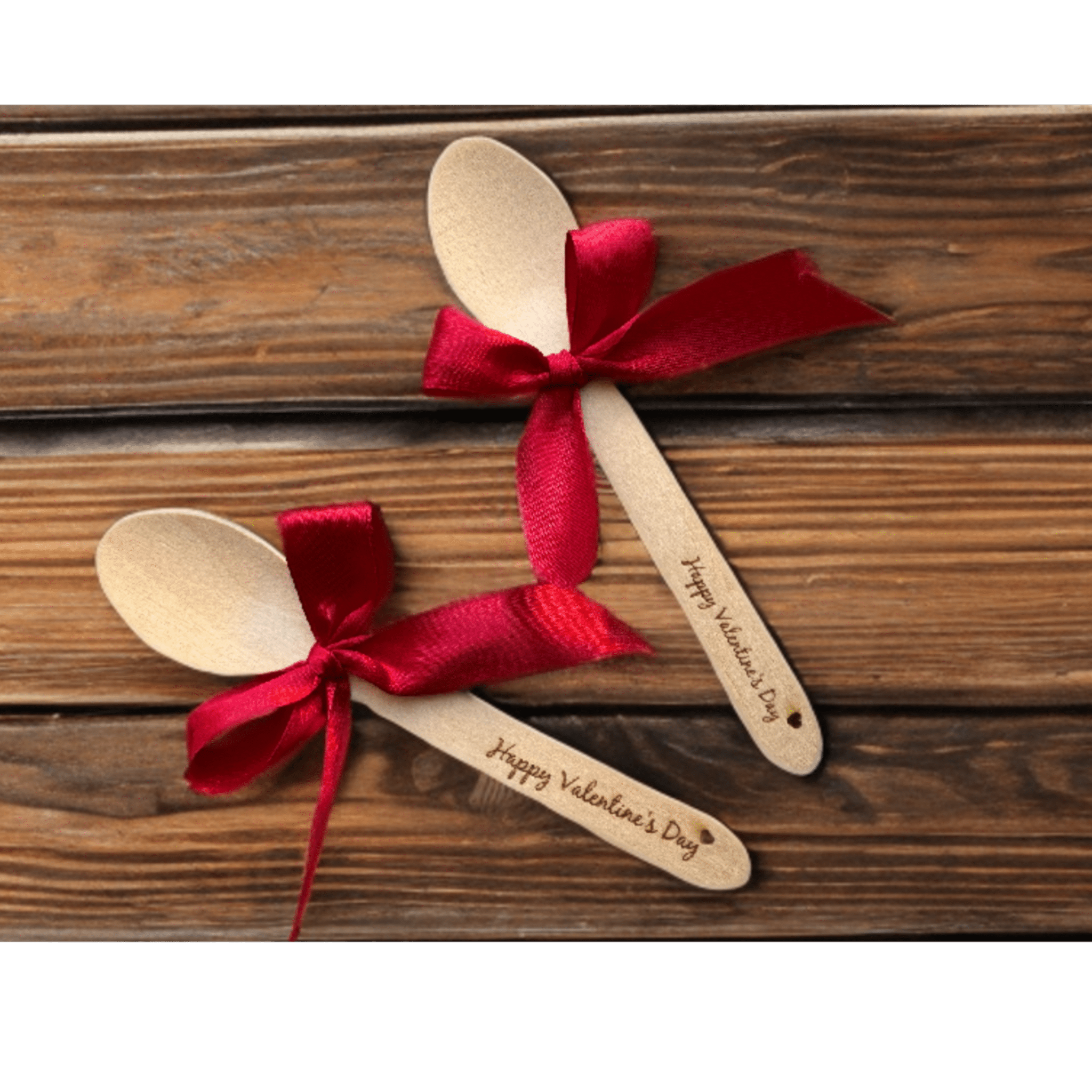 Two engraved wooden spoons with red ribbon bows on a wooden surface – personalised wooden spoons – Etch 'N' Shine