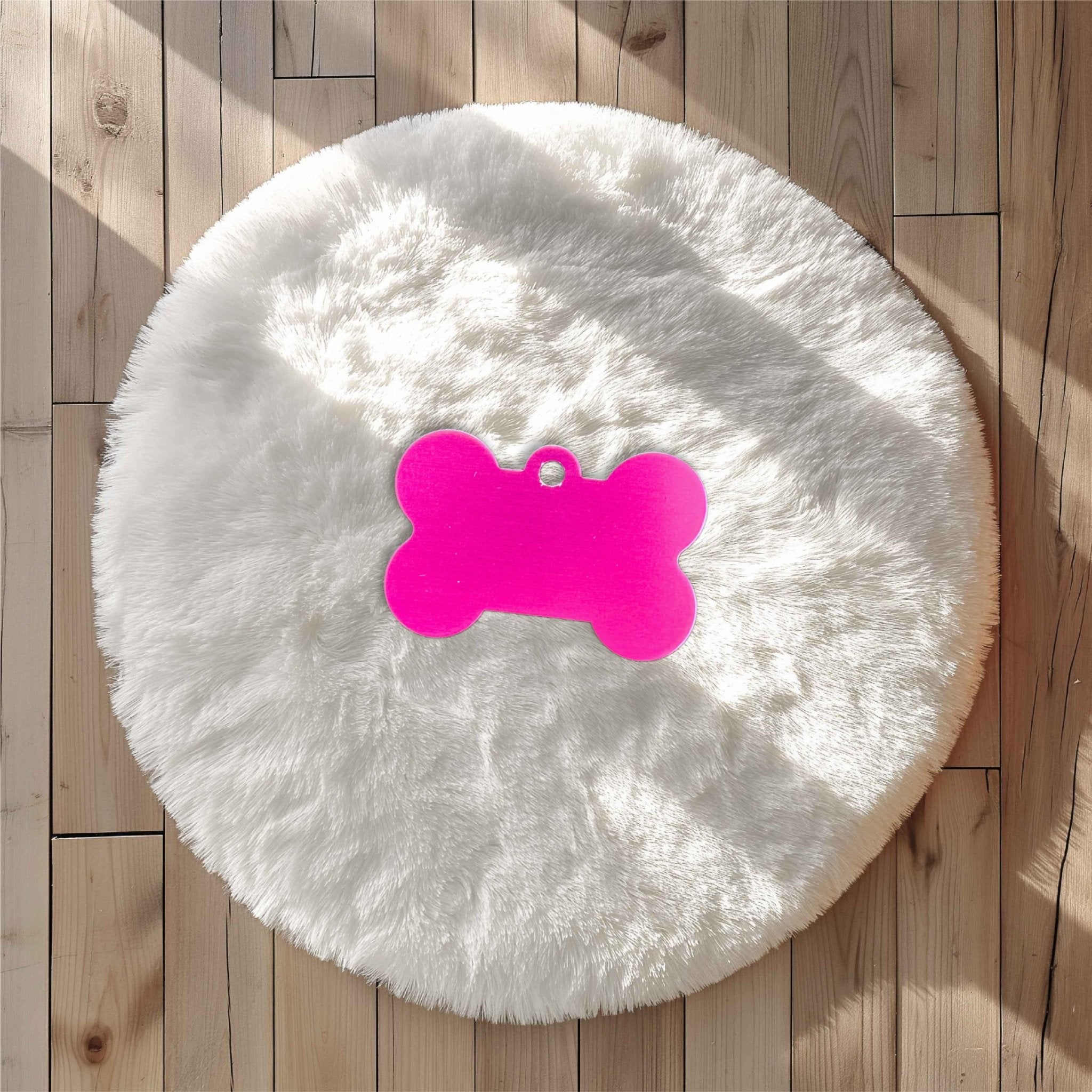 Pink bone-shaped pet tag on a white fluffy surface – personalised engraved metal pet name tag – Etch 'N' Shine