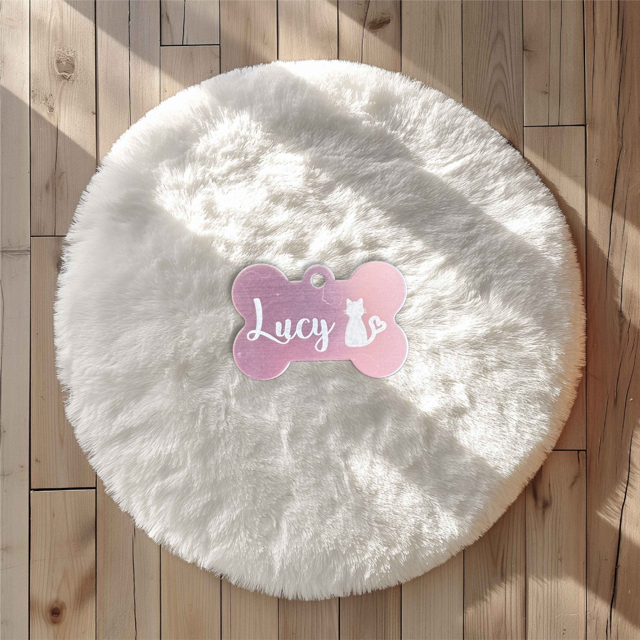 Pink bone-shaped pet tag with custom name and cat motif on a round fluffy pet bed – engraved metal pet tag – Etch 'N' Shine