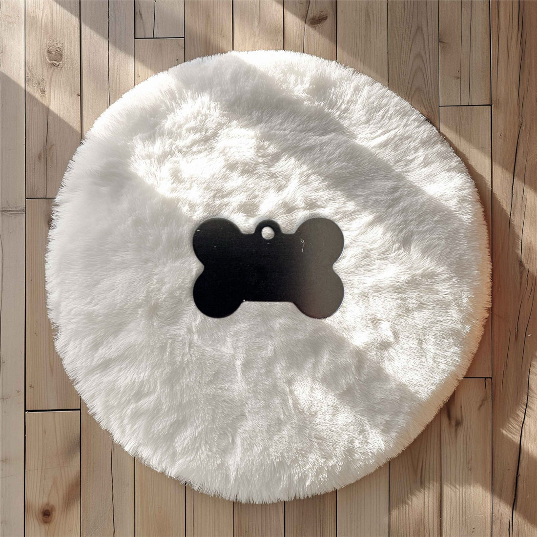 Black bone-shaped pet tag on a white faux fur surface on wooden flooring – engraved metal pet name tag – Etch 'N' Shine