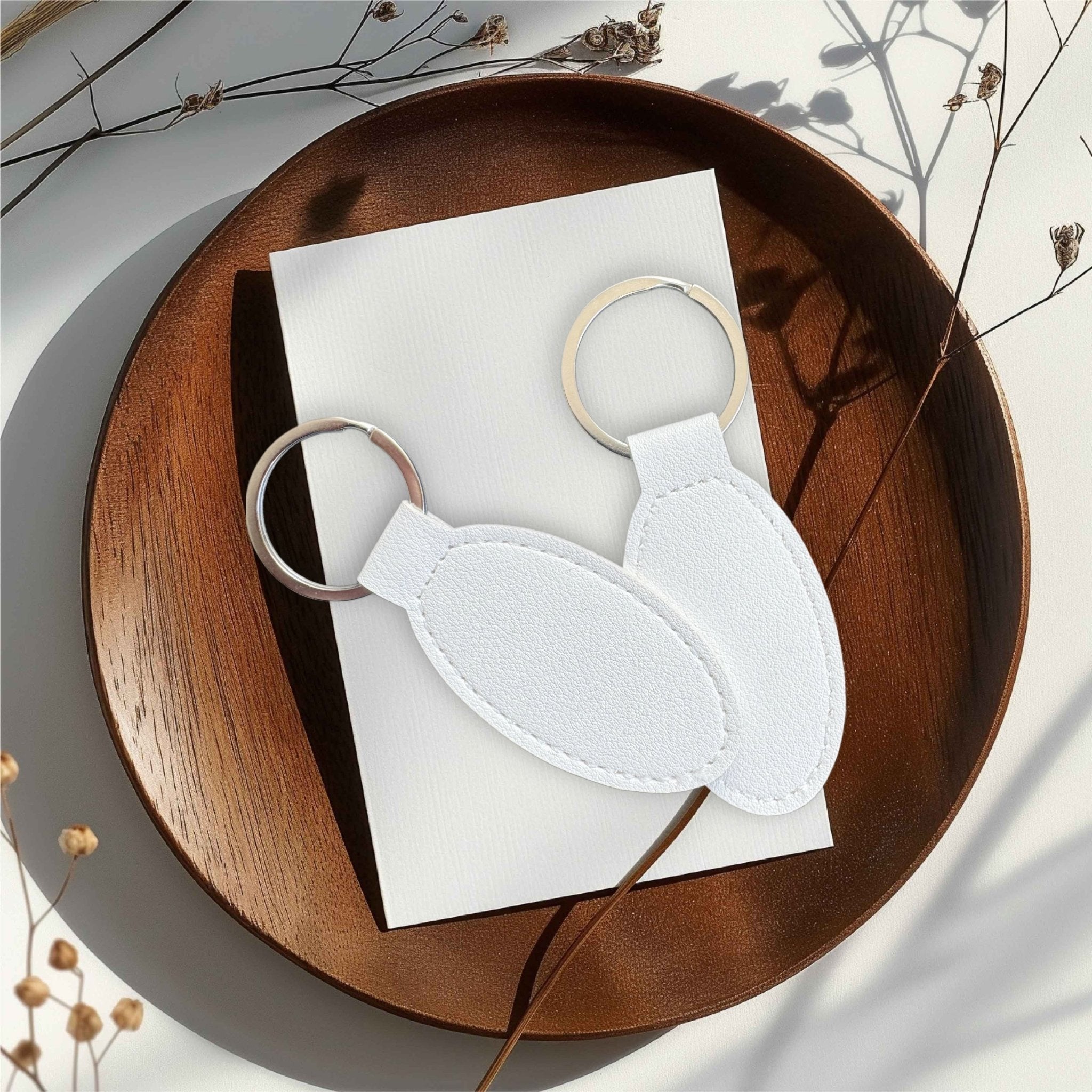 Two white oval keyrings on a wooden tray – personalised engraved PU leather keyring – Etch 'N' Shine