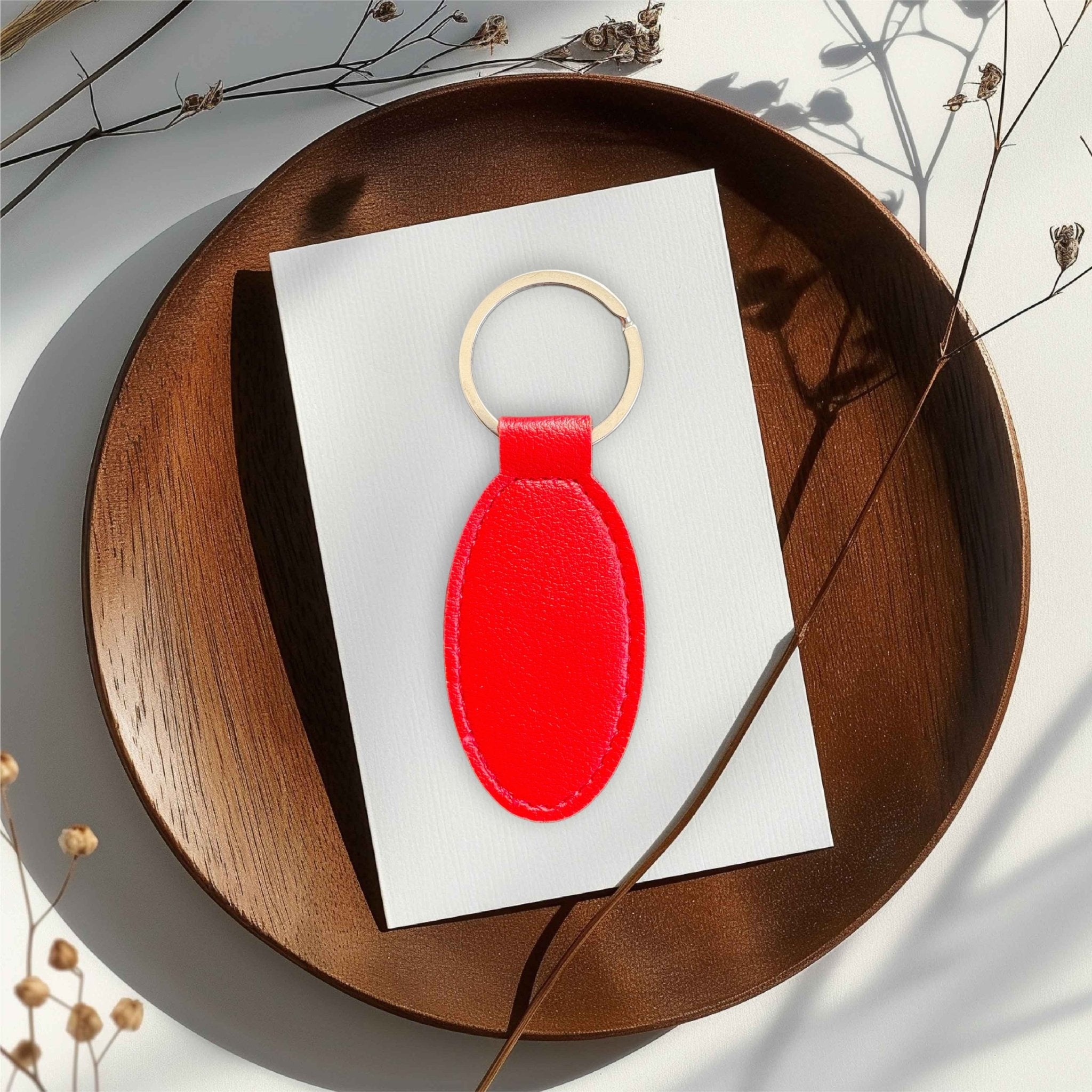 Red oval PU leather keyring on a white card atop a wooden tray – personalised engraved leather keyring – Etch 'N' Shine