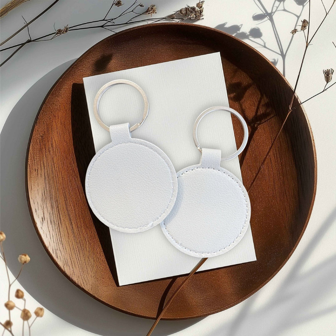 Two round white leather keyrings on a wooden tray – personalised PU leather keyring – Etch 'N' Shine