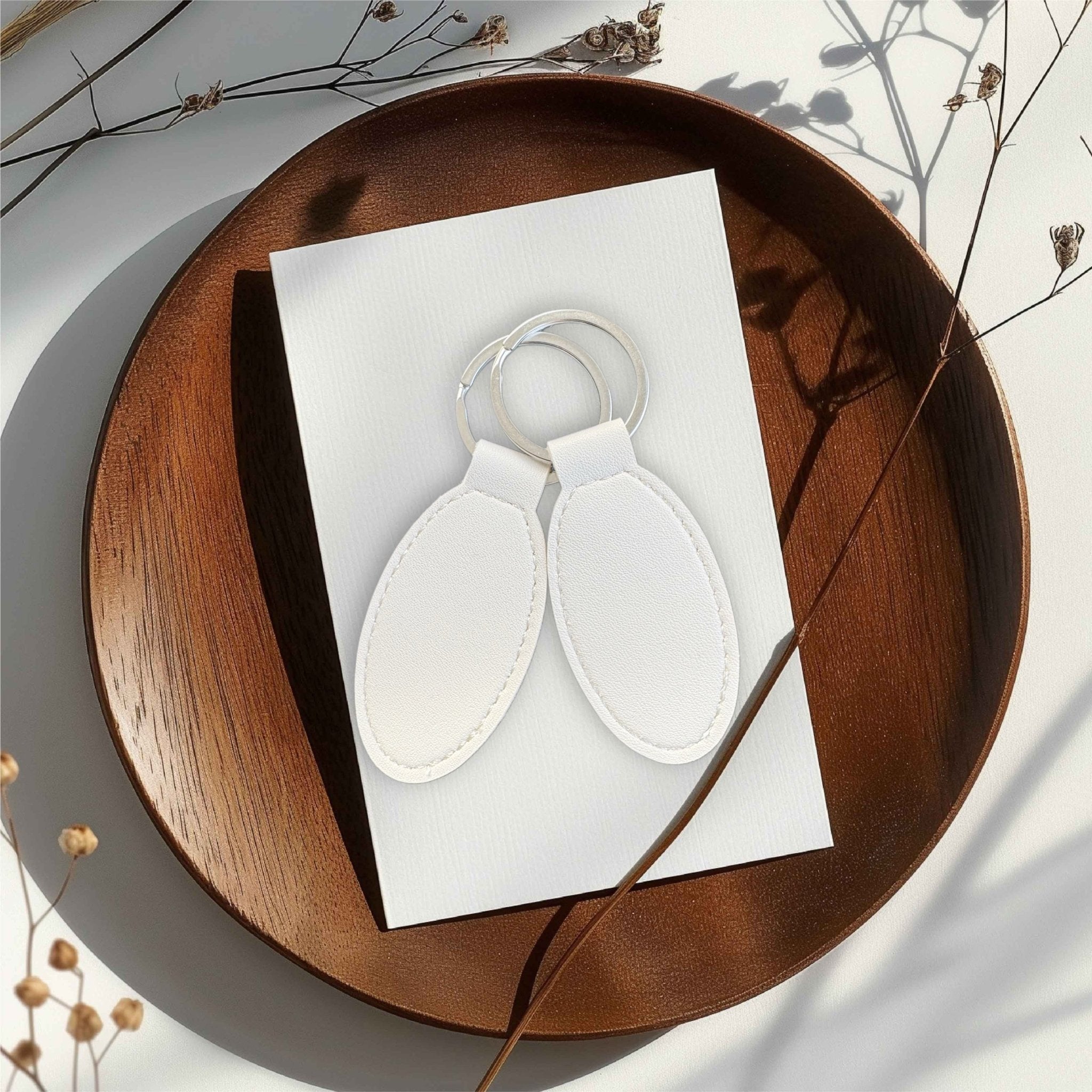 Two white oval keyrings on a wooden tray – personalised engraved PU leather keyring – Etch 'N' Shine