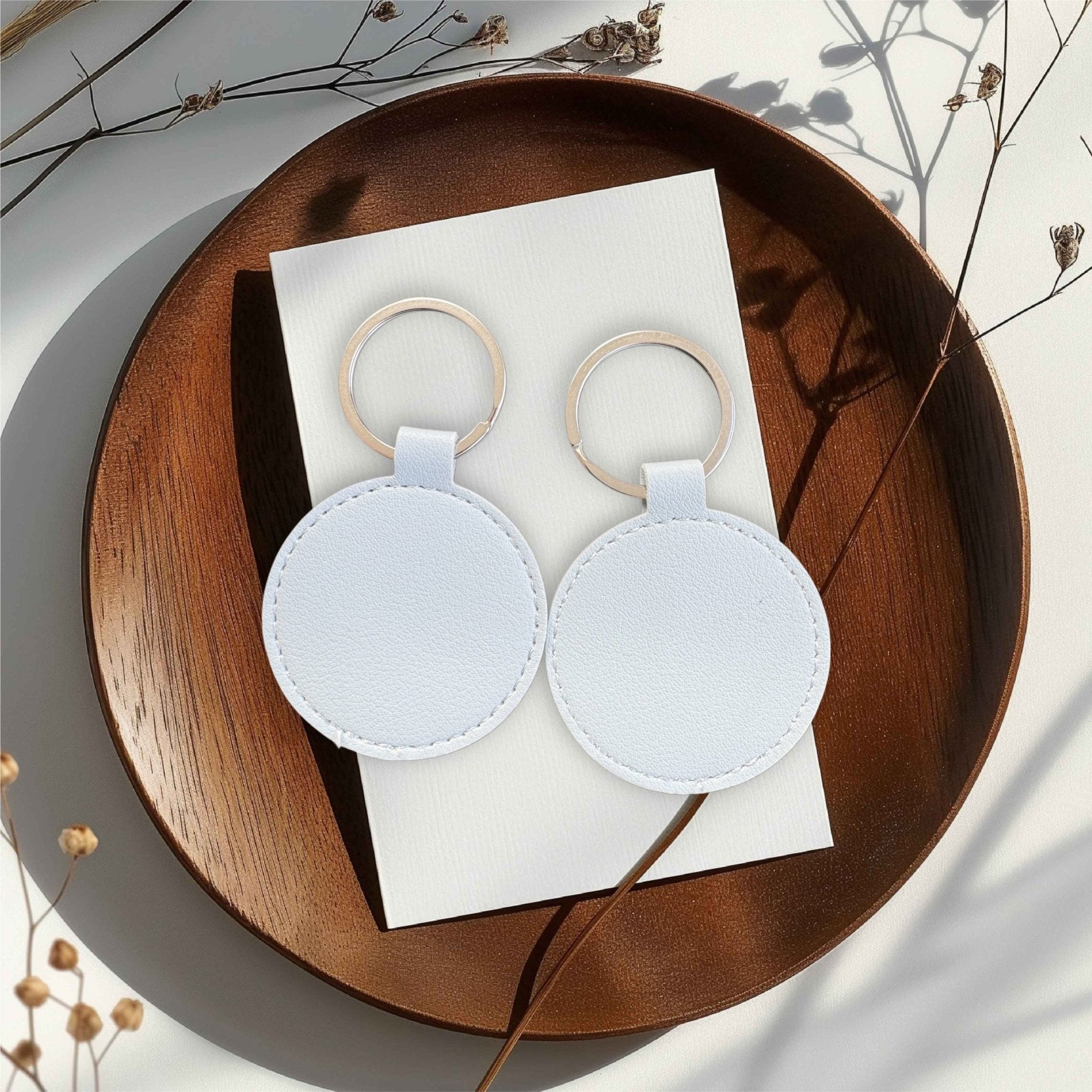 Two white round keyrings on a wooden tray – personalised engraved PU leather keyring – Etch 'N' Shine