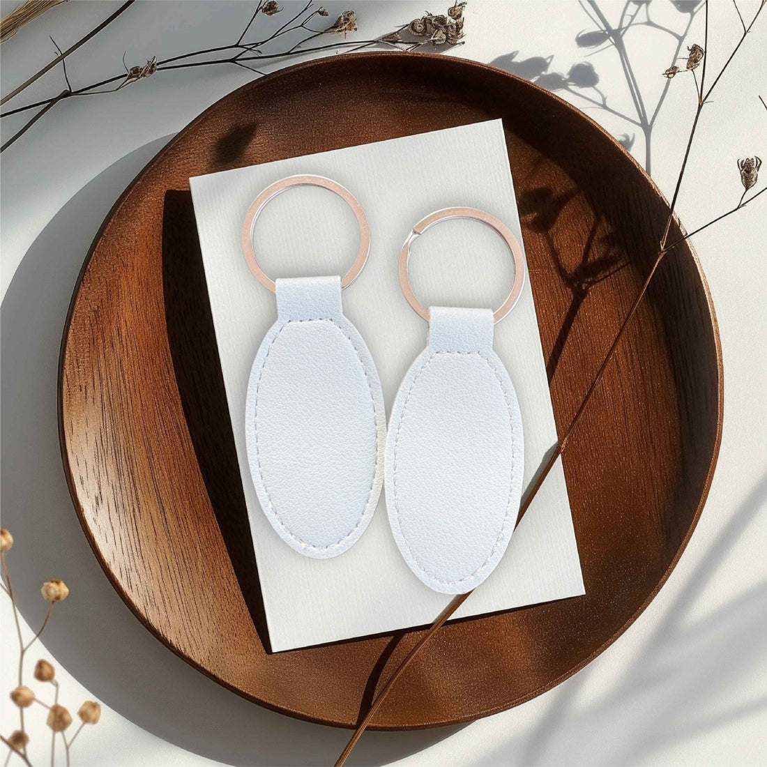 Two white oval leather keyrings on a wooden tray – personalised engraved PU leather keyring – Etch 'N' Shine