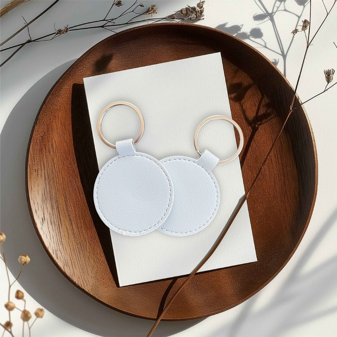 Two round white leather keyrings on a wooden tray – personalised engraved PU leather keyring – Etch 'N' Shine